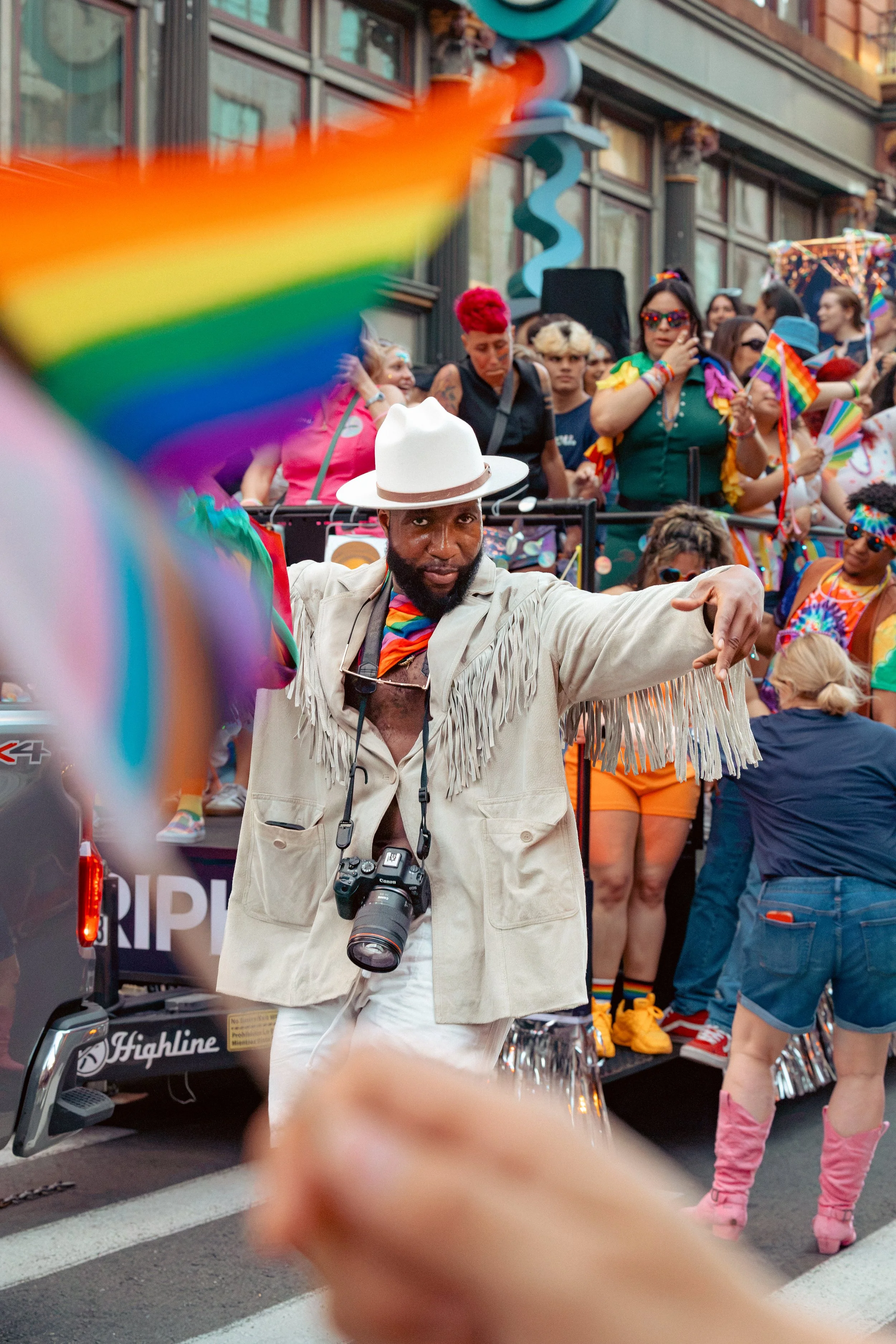 A group of people participating in a pride parade, with rainbow flags and colorful outfits, standing on a float and walking on the street.