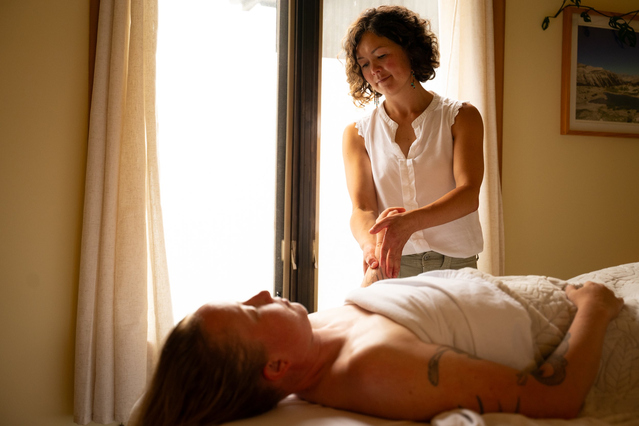 Female client laying on back, having her left hand massaged by therapist