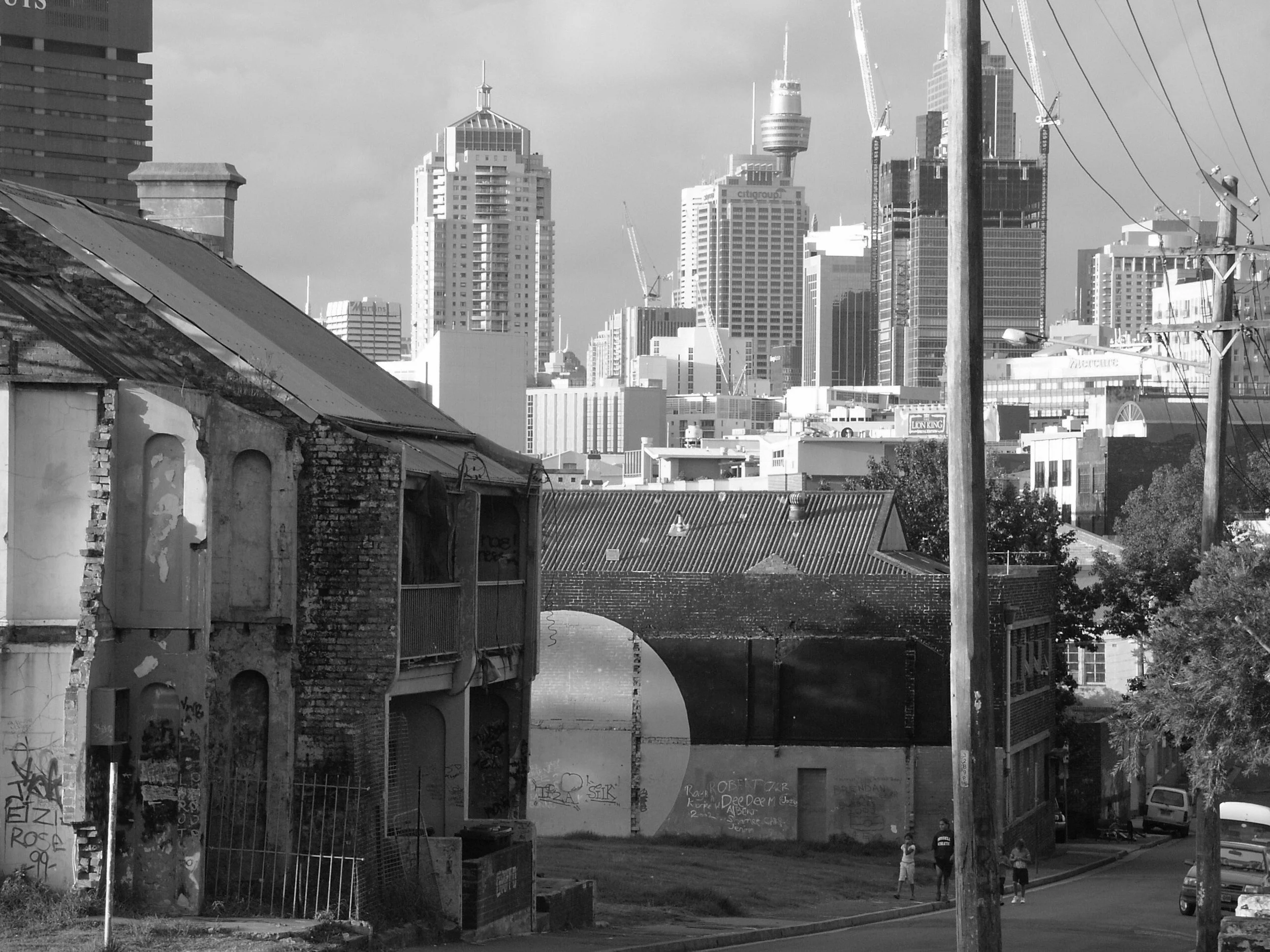 Black and white photo showing 'The Block' in Redfern, Sydney  in the background, with an urban skyline and skyscrapers in the background.
