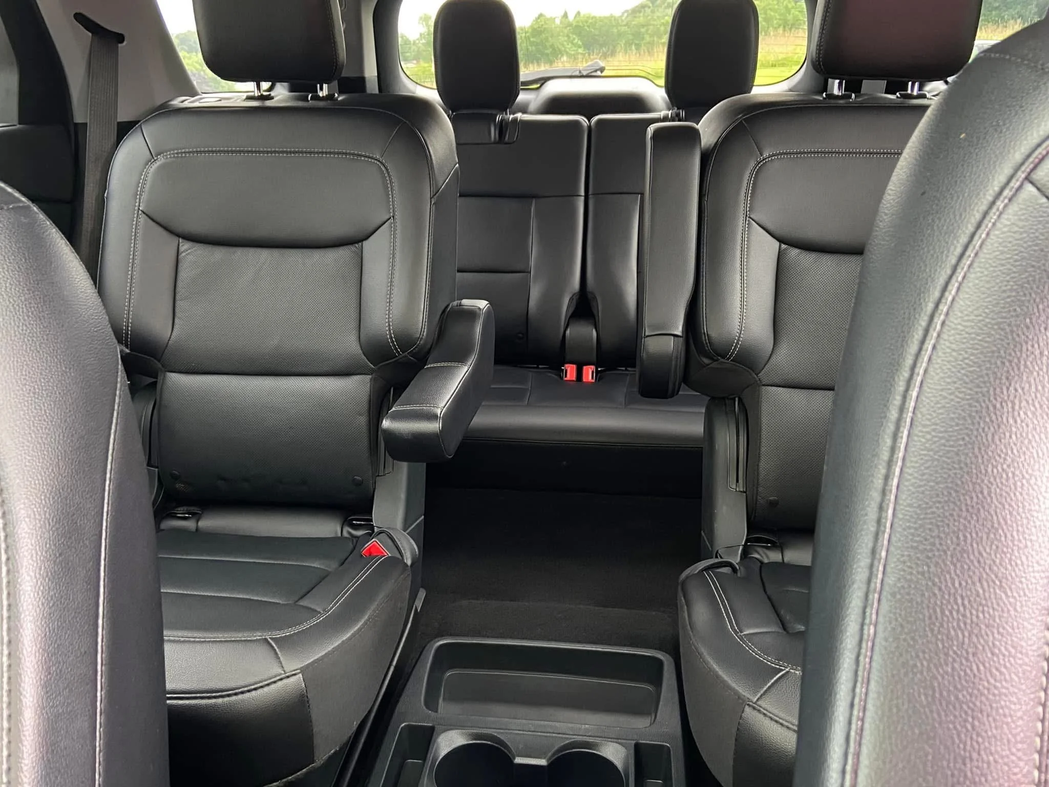Interior of a vehicle showing three rows of black leather seats, with the middle row featuring captain's chairs, and the third row folded up in the background.