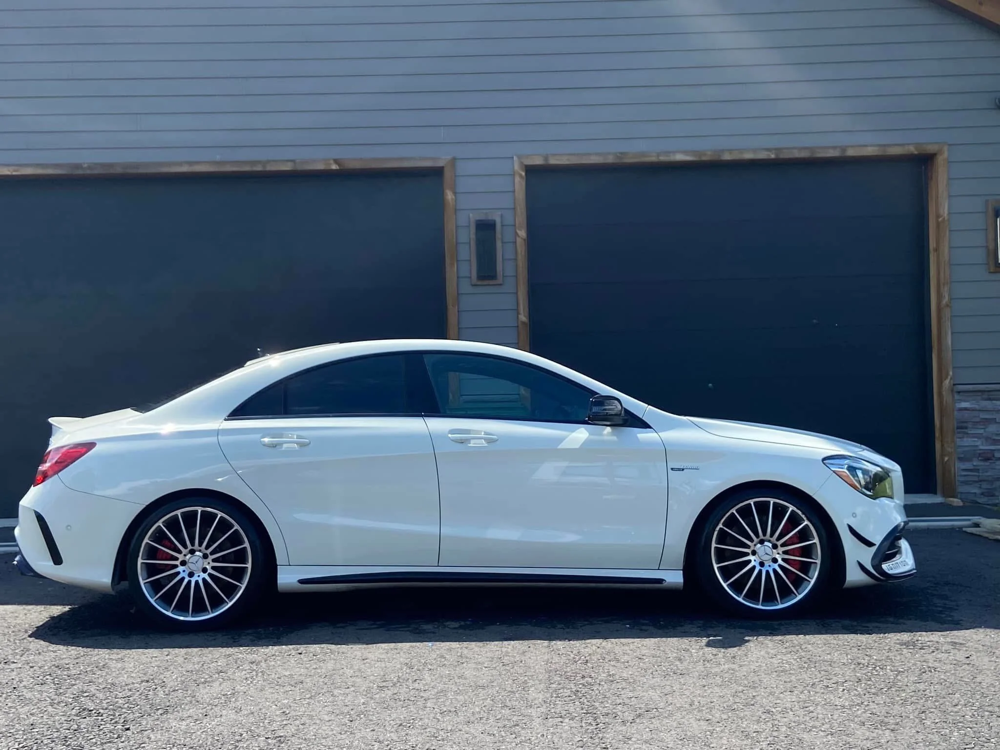 White luxury sedan parked in front of a modern house with dark garage doors and blue siding.