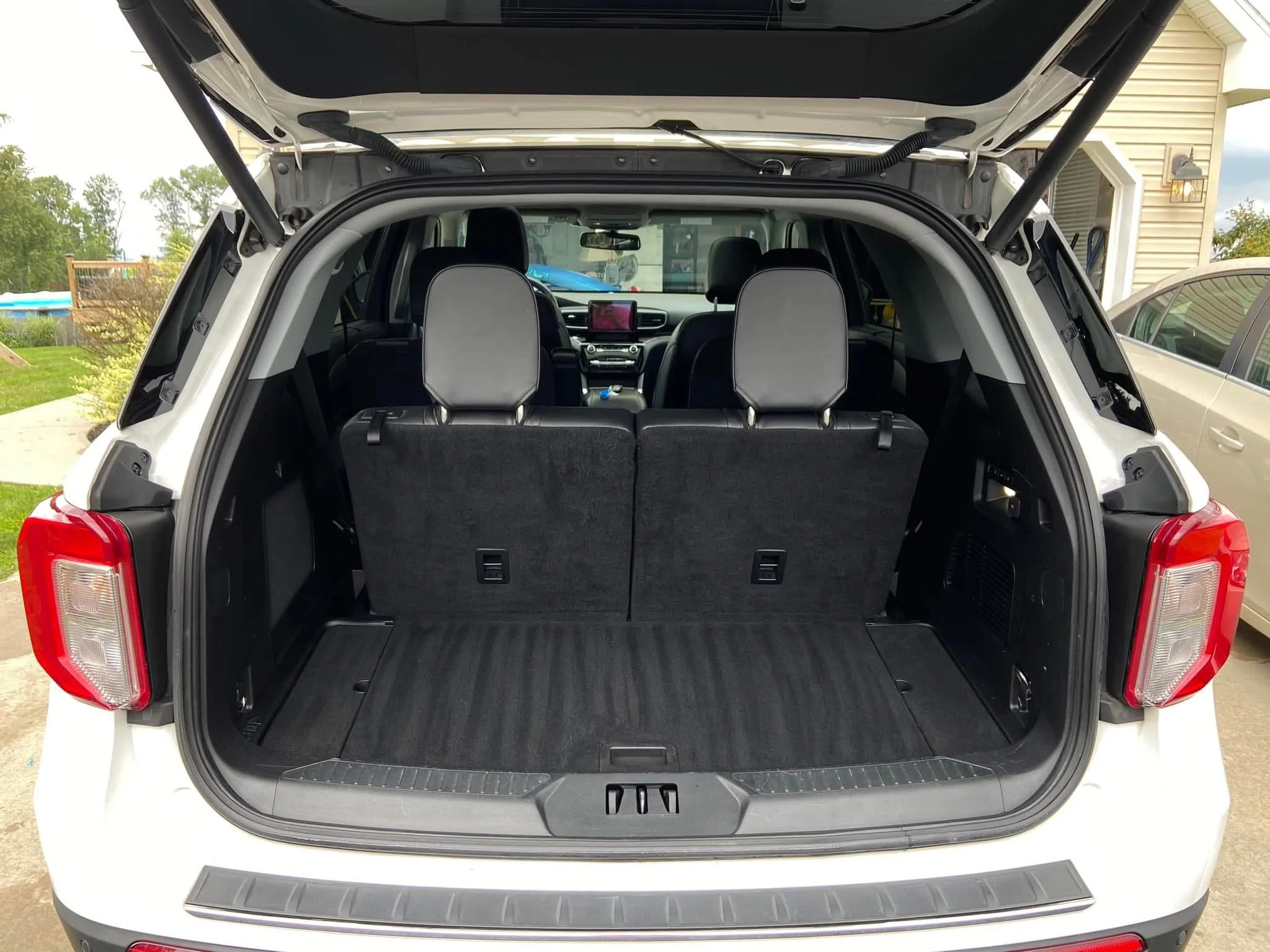 Open trunk of a white SUV showing black interior with the rear seats in an upright position and a view of the dashboard through the windshield.