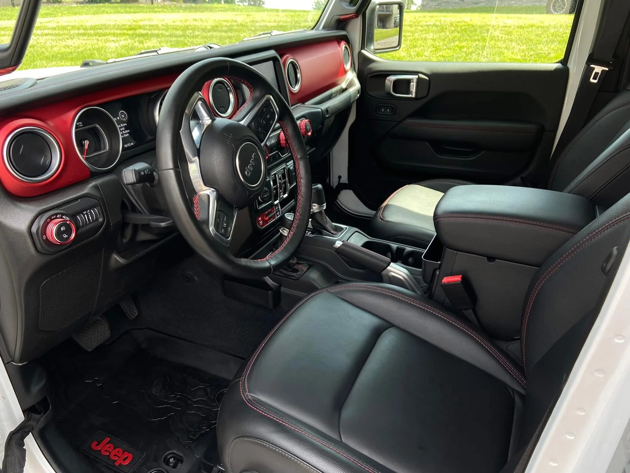 The interior of a Jeep with a red-themed dashboard, black leather seats with red stitching, and a center console.