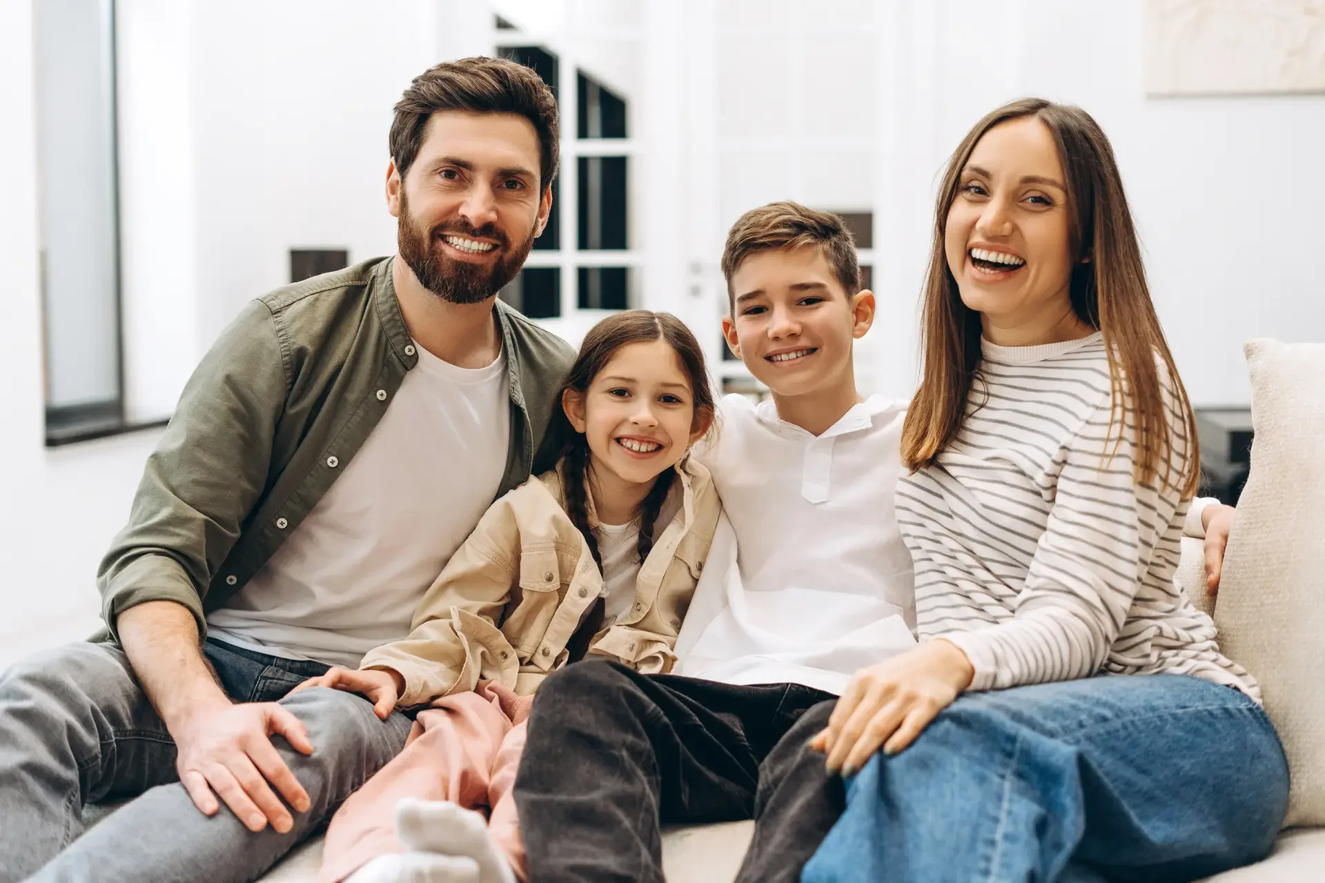A happy family of four sitting on a couch in a modern living room, smiling at the camera.
