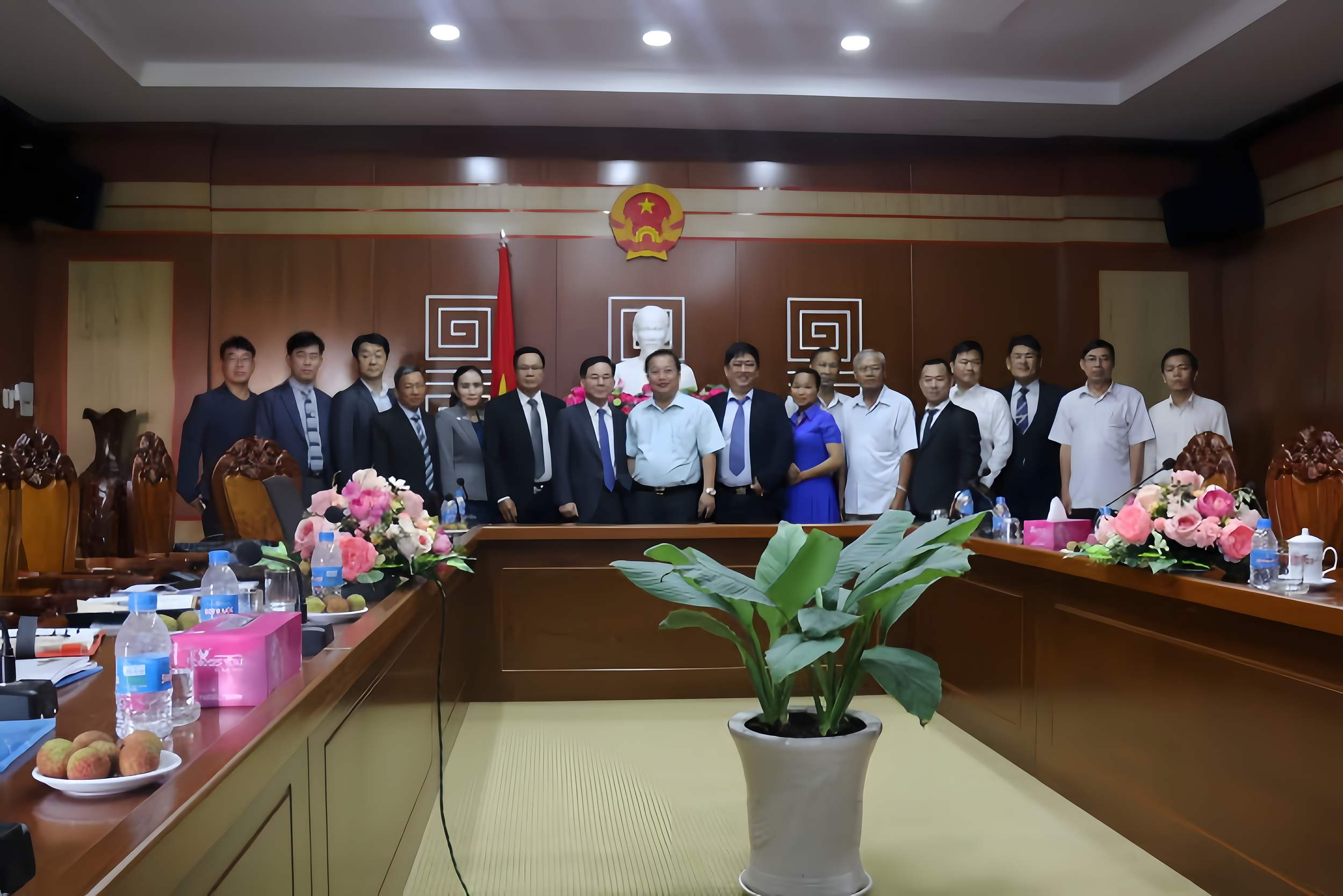 Group of people standing in a conference room with a bust, flowers, and the flag of Vietnam behind them.