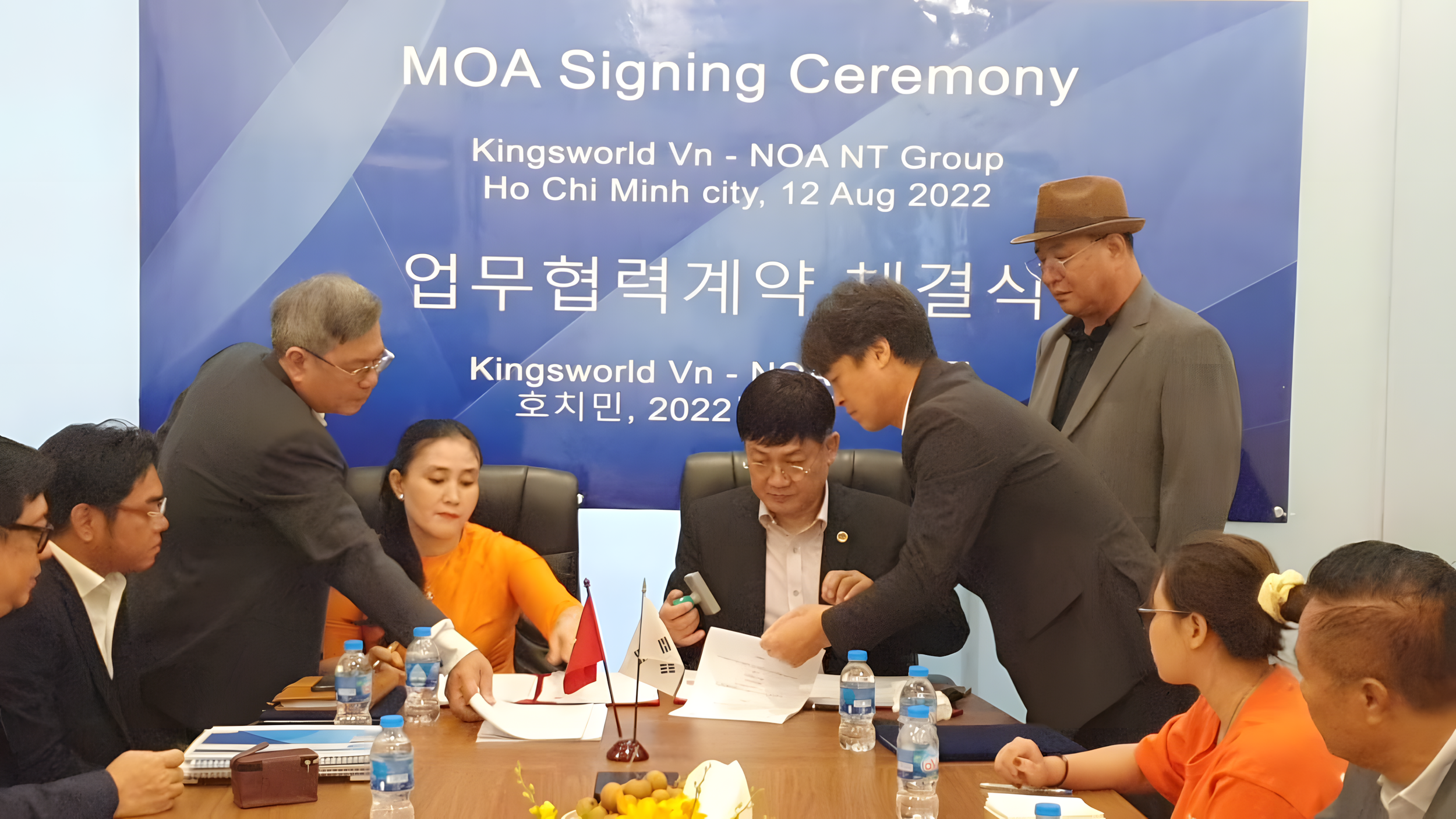 A group of people at a signing ceremony for a memorandum of agreement, seated at a table with flags of South Korea and Vietnam, in front of a blue backdrop with text about the event held in Ho Chi Minh City on August 12, 2022.