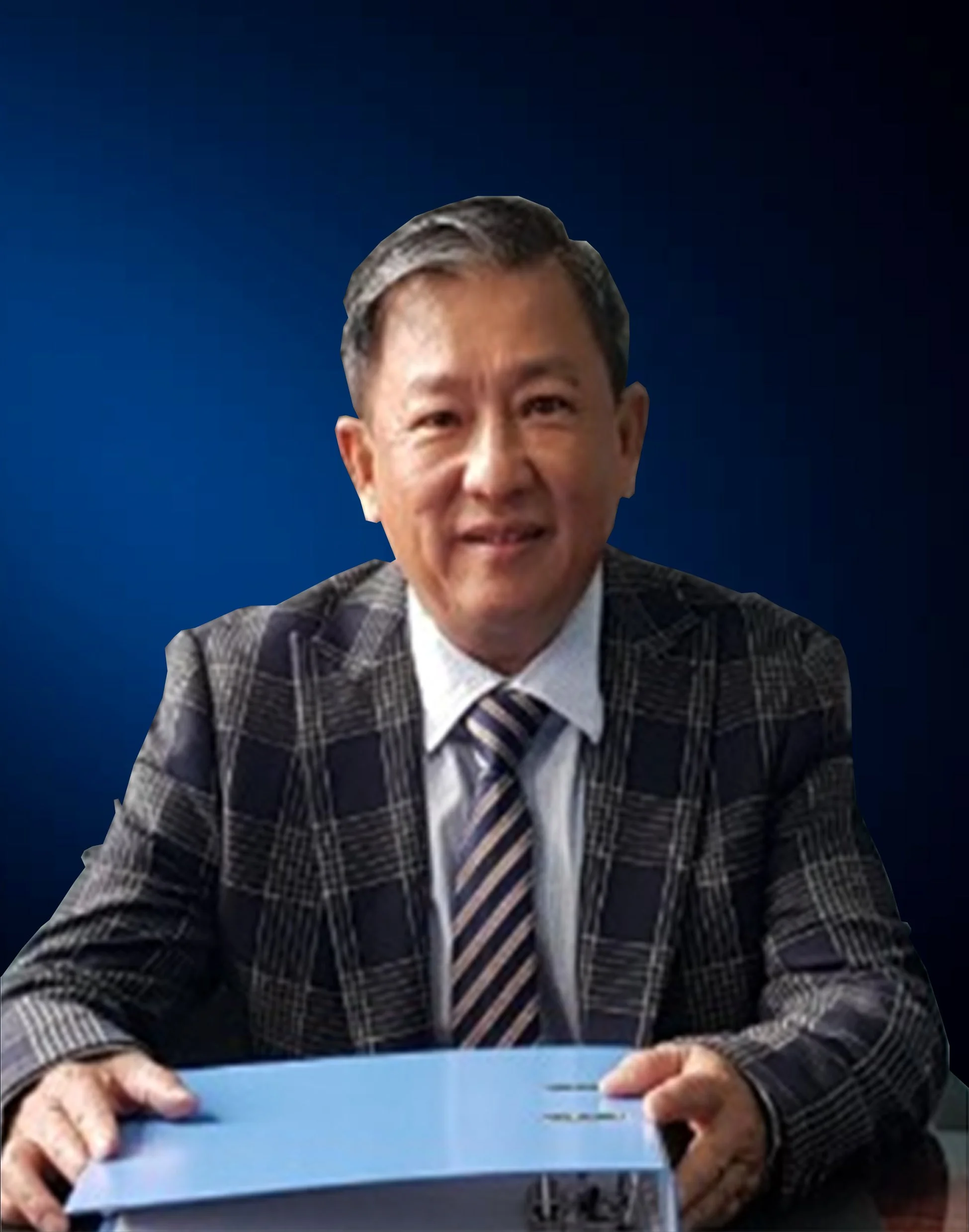 A middle-aged man in a checkered suit with a striped tie, sitting at a table with a blue folder, smiling at the camera against a dark blue background.