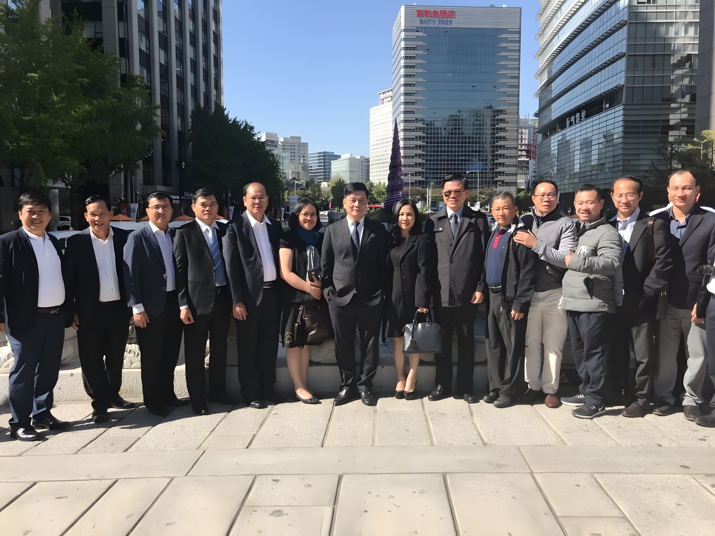 A group of professionals dressed in business attire standing on a city sidewalk with tall buildings in the background.