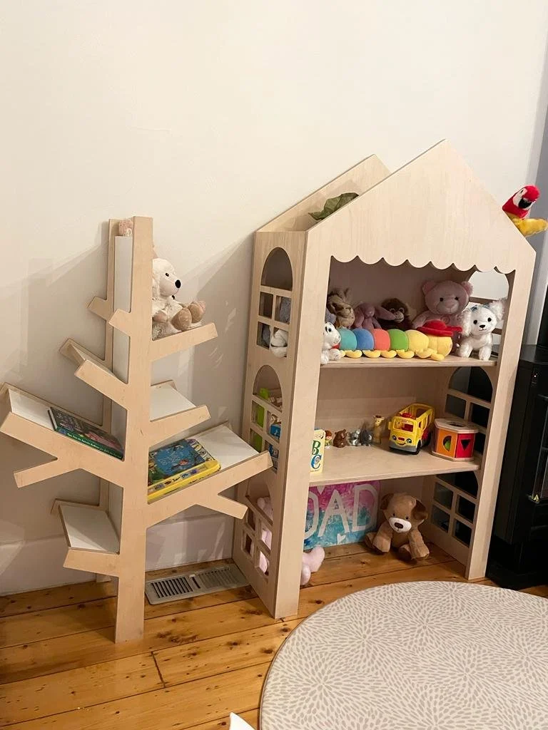 Freestanding dollhouse display shelf made from raw birch plywood with window cut-outs and scalloped trim. Features 3 shelves and pitched roof design. Ideal for events, kids’ rooms, or markets.