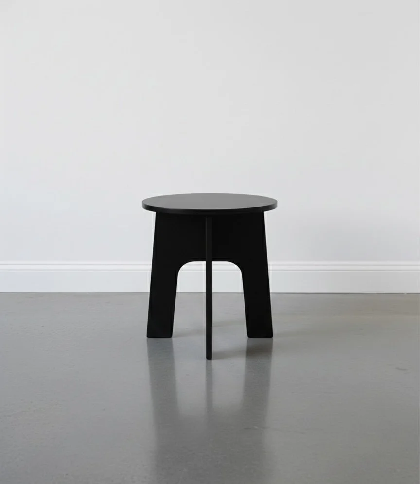 Lightweight folding stool painted black in a studio with white wall and polished concrete floor