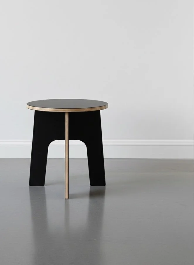 Marine grade plywood outdoor collapsible stool in a well lit studio with white wall and concrete floor