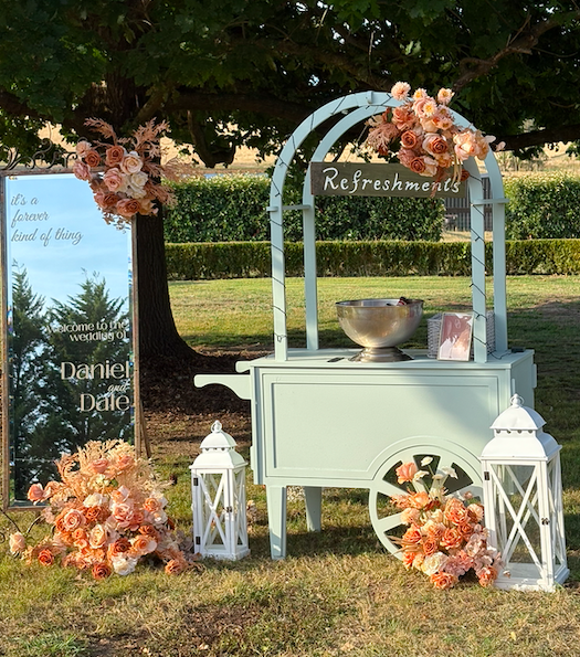 Sage green collapsible cart with long brass handle and cream fringe canopy. Ideal for styled pop-ups, wedding bars, and market displays. Click-together design, available to hire in Melbourne.