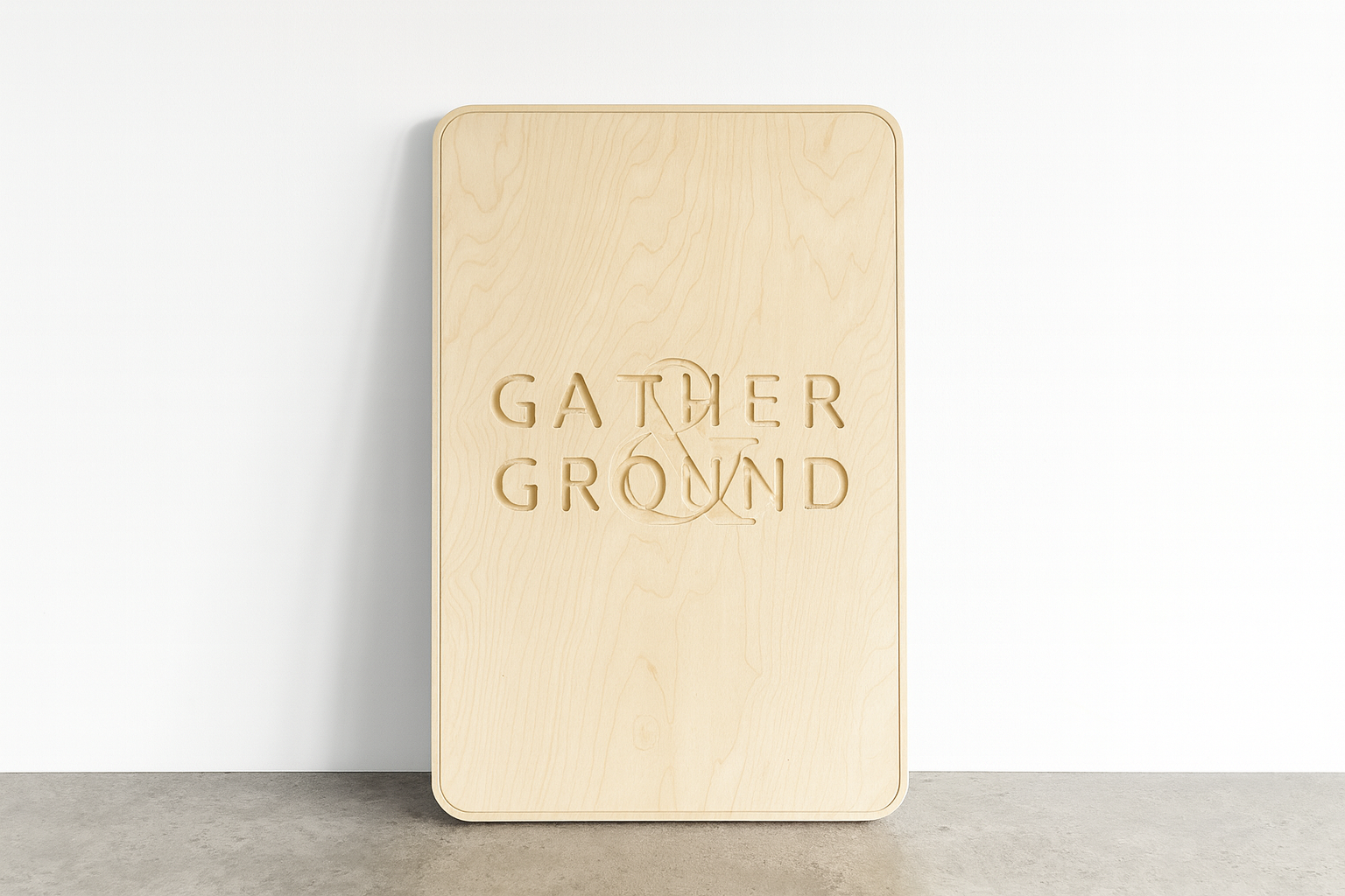 A wooden sign with the words "Gather & Ground" carved into it, leaning against a white wall.