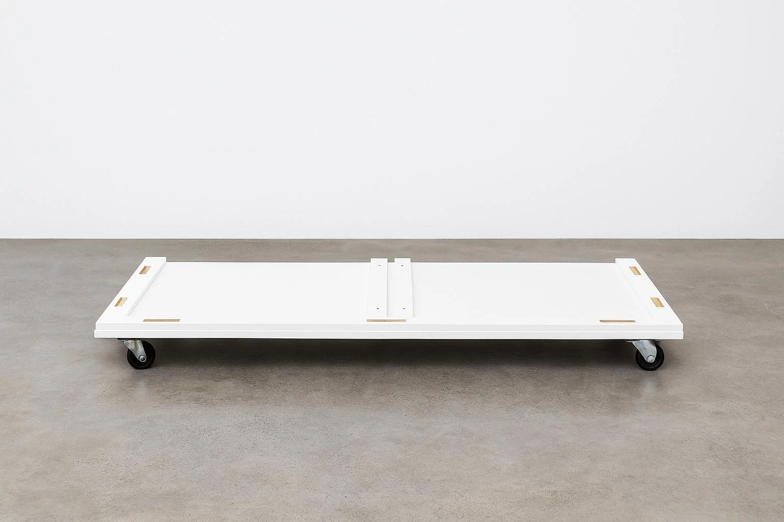 Minimalist white platform on wheels against a plain white wall.