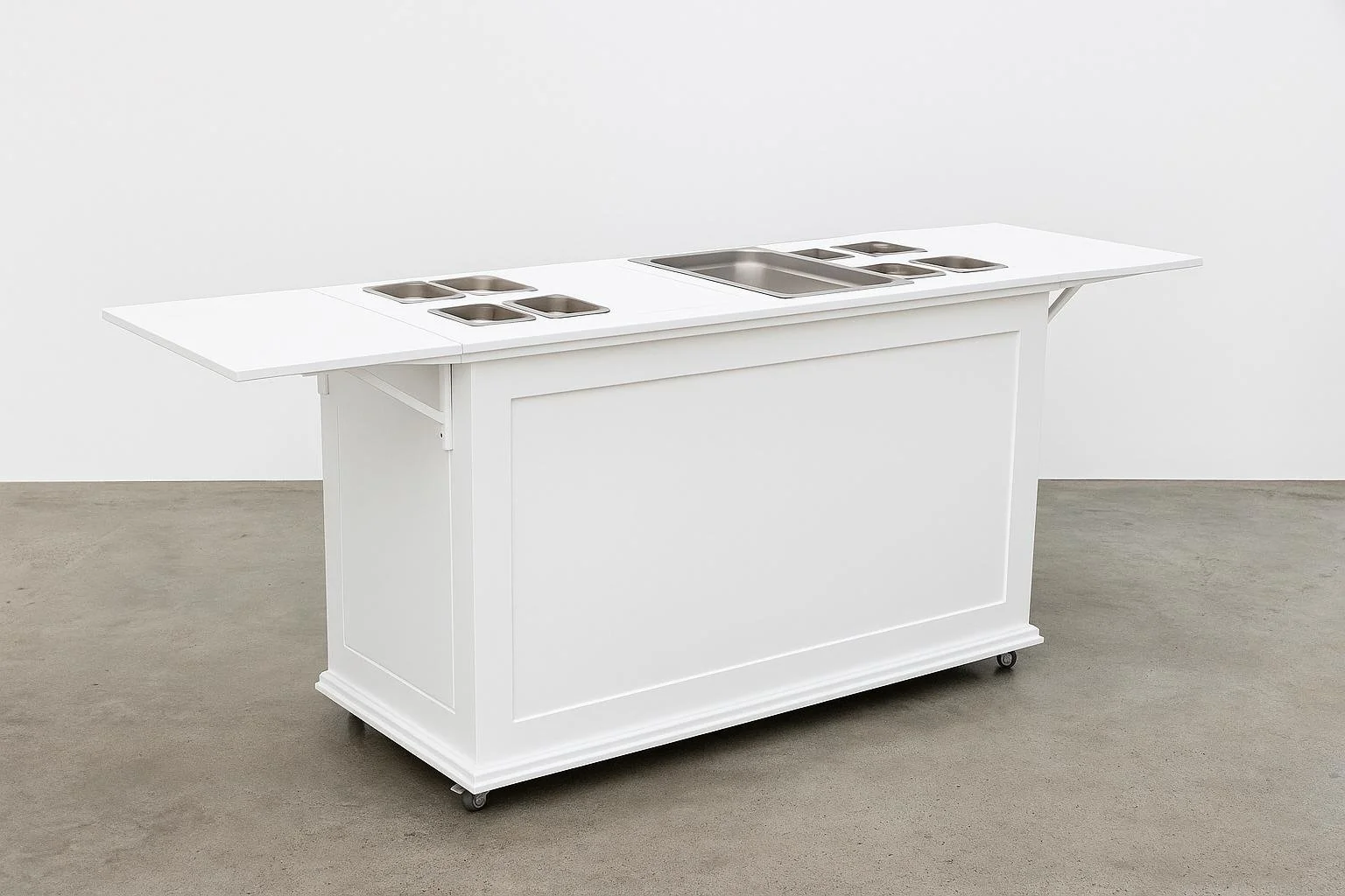 White mobile food serving counter with stainless steel compartments for food trays, set on a concrete floor against a plain white wall.