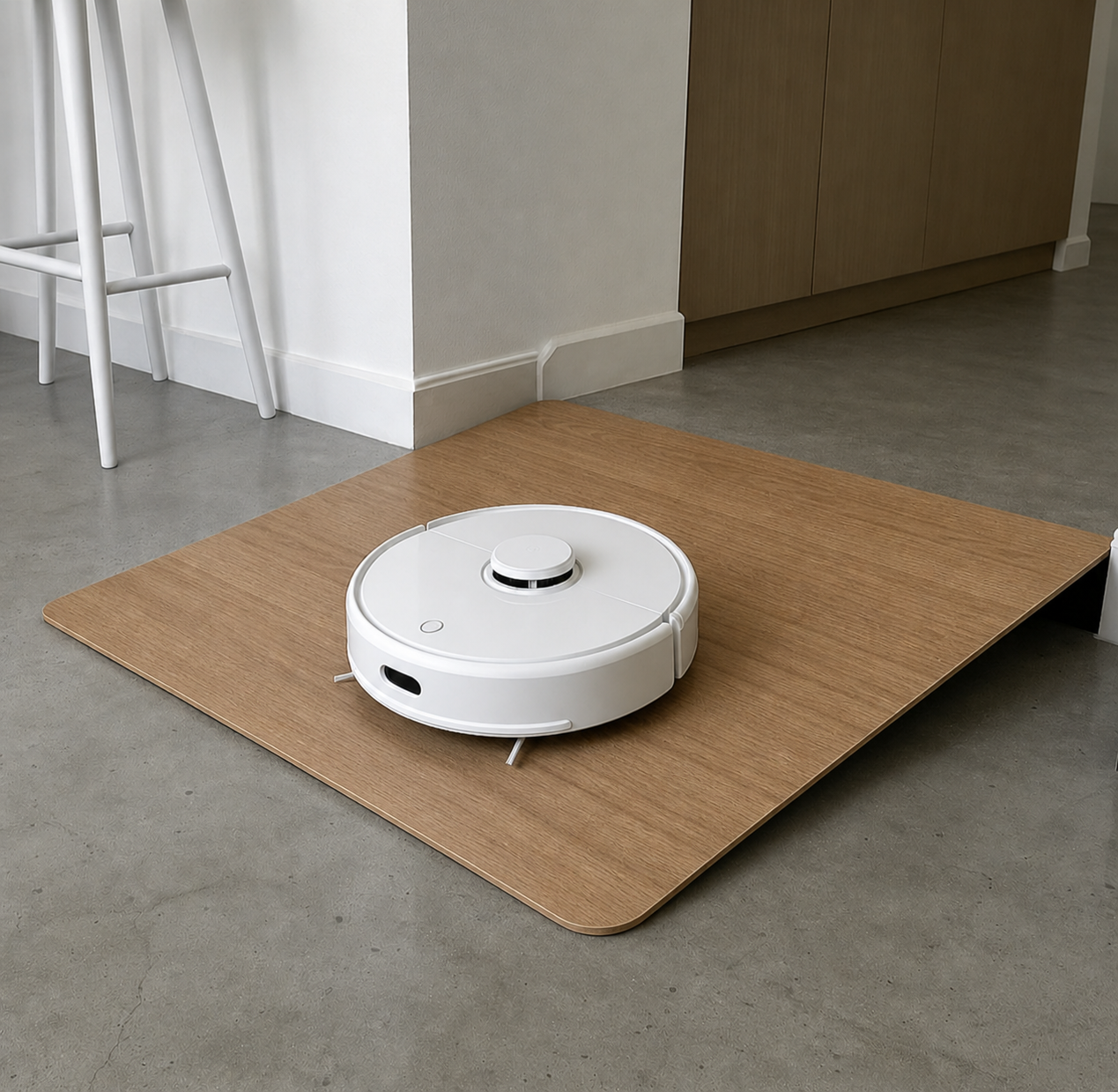 A white robotic vacuum cleaner on a wooden floor mat in a modern kitchen.