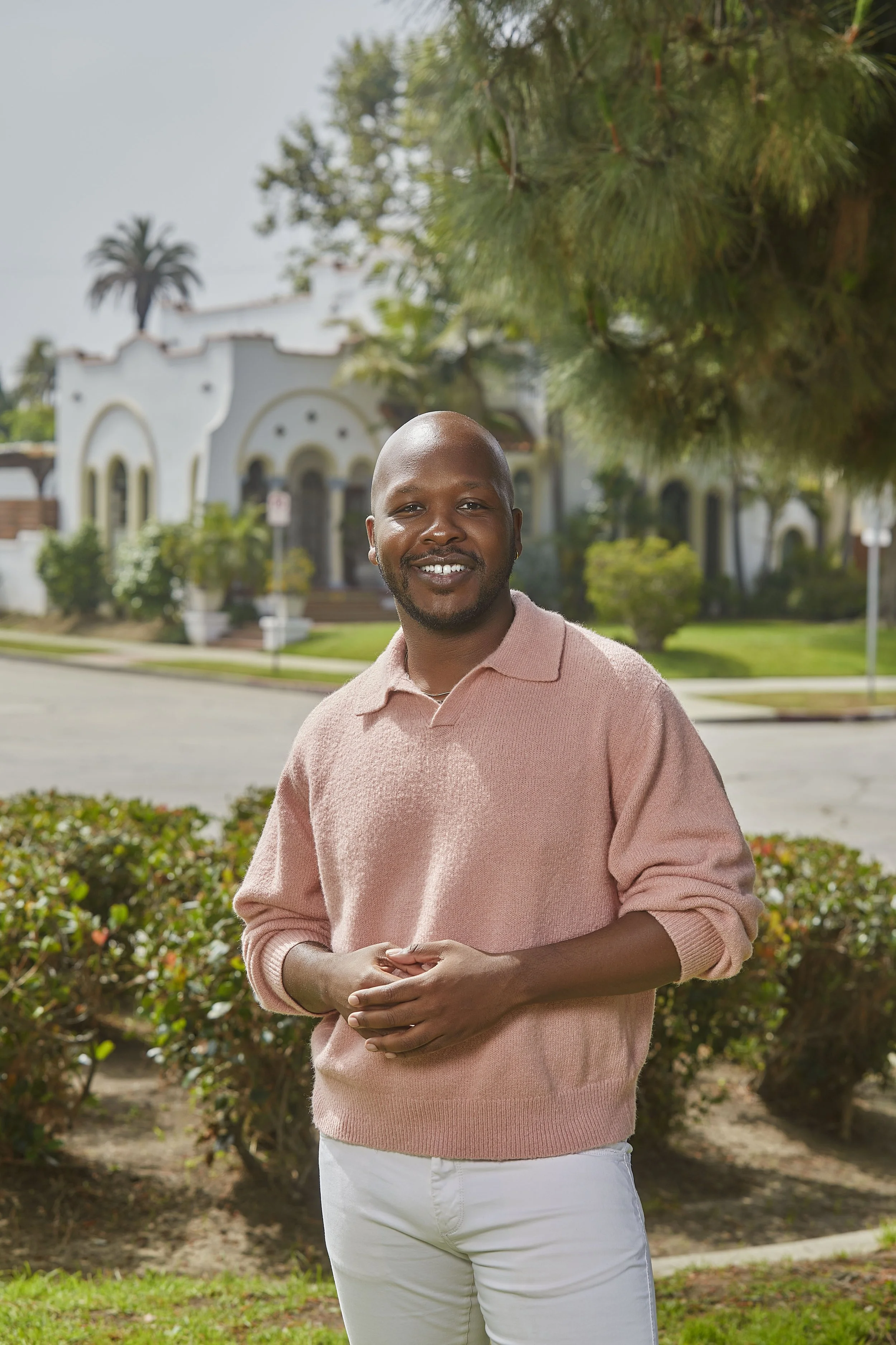 Nich Banks, Compass REALTOR® in Los Angeles, standing outdoors in a pink sweater with a residential neighborhood in the background.