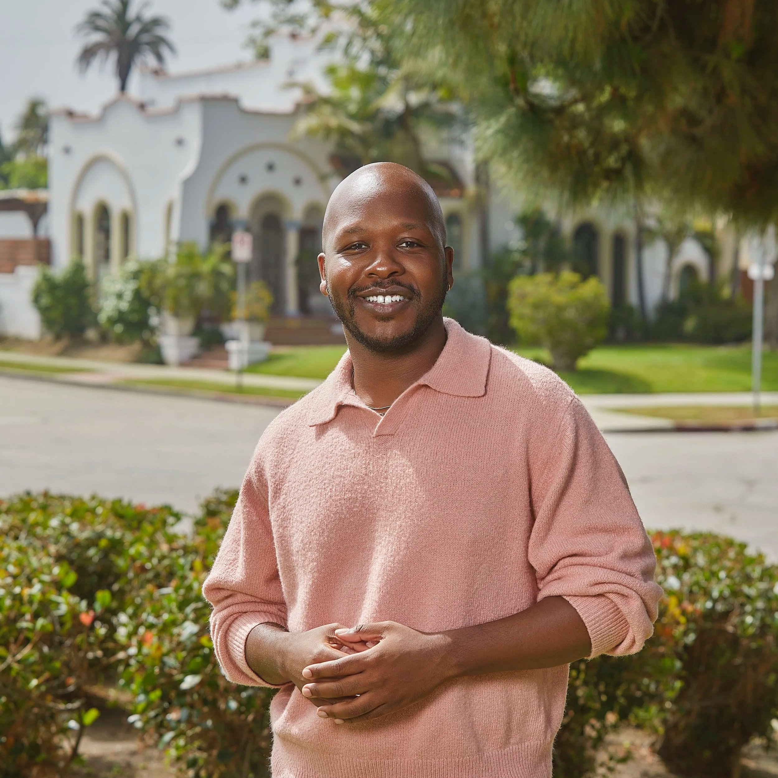 Los Angeles REALTOR® Nich Banks smiling in a pink sweater, standing in front of a landscaped residential property.