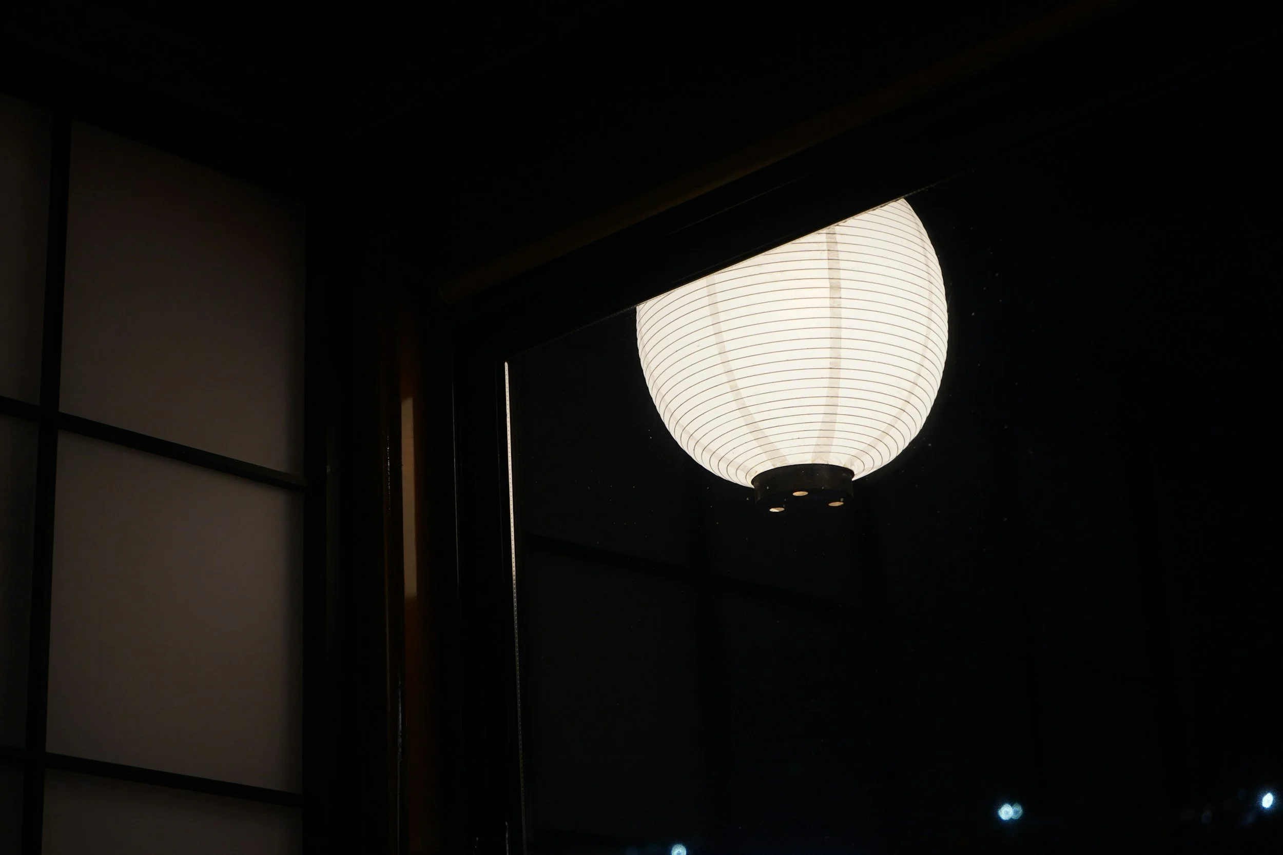 A paper lantern hanging outside at night, viewed through a window.