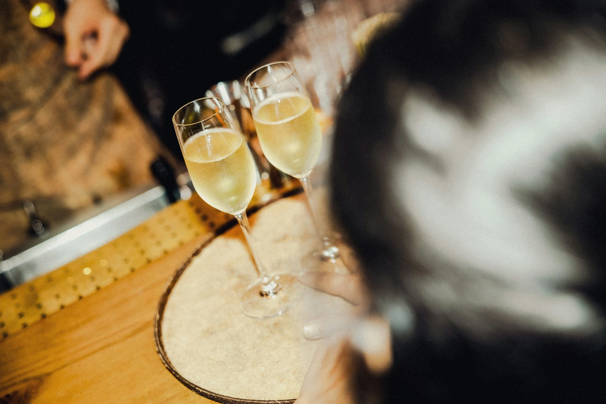 Two glasses of champagne on a wooden bar counter.