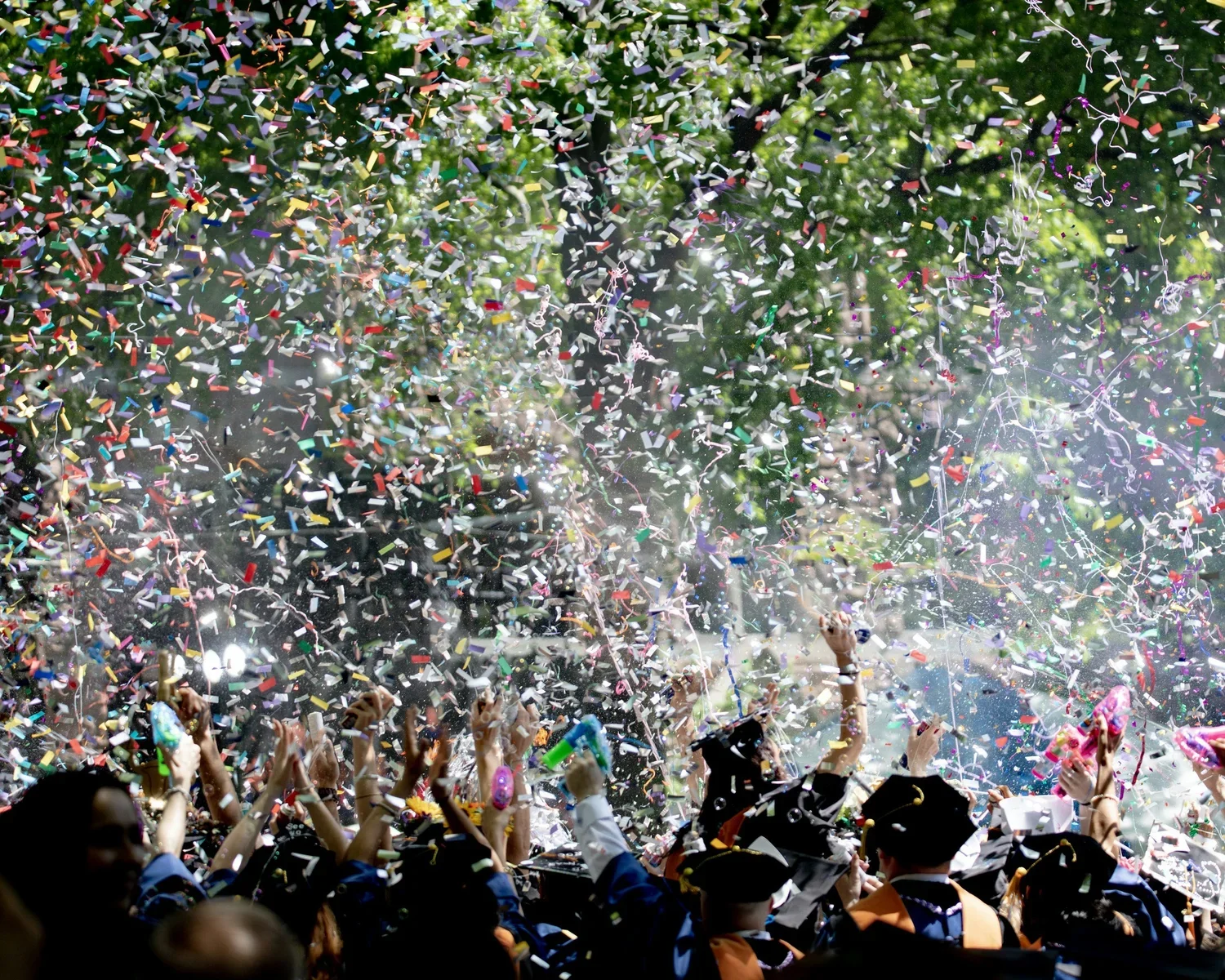 Graduates celebrating at a graduation ceremony with colorful confetti raining down.