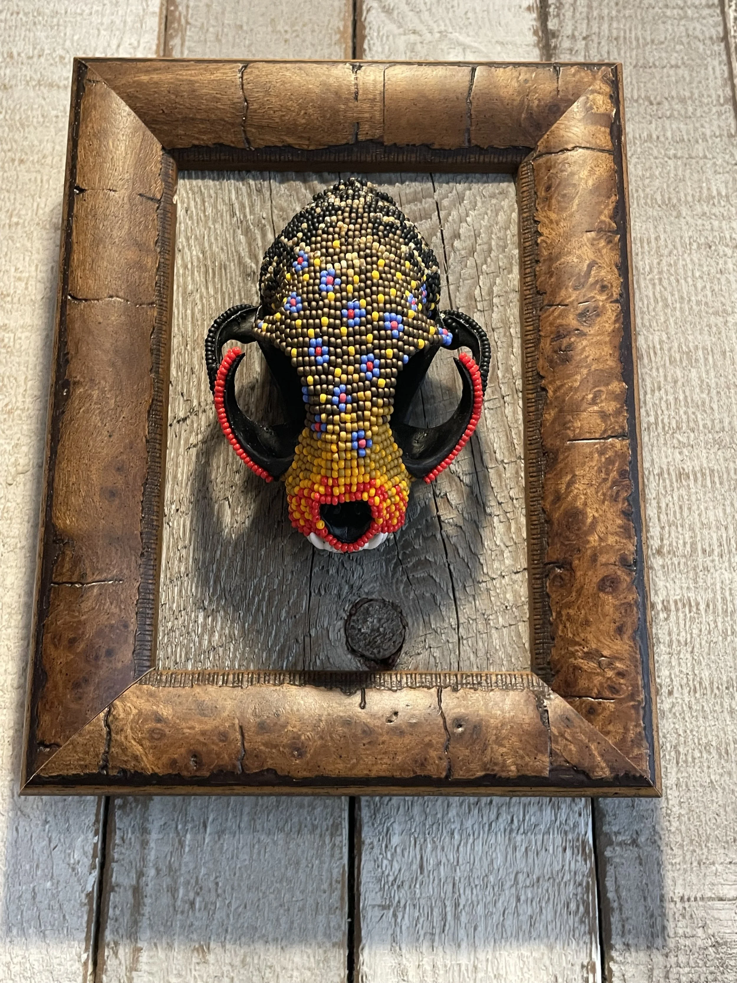 Beaded animal skull wall art framed in wood, displayed on wooden surface.