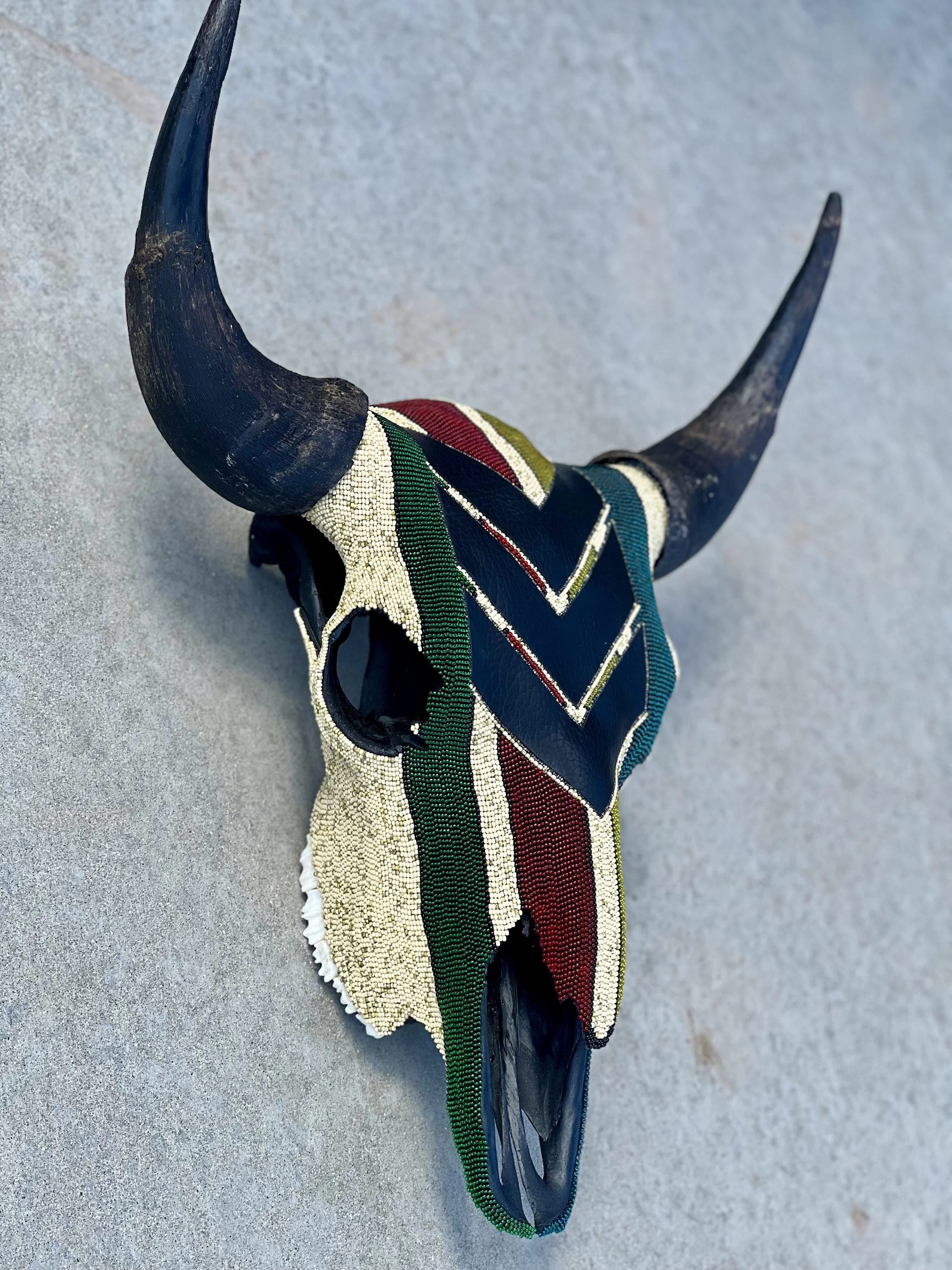 Decorative bison skull with large curved horns, decorated with colorful beaded patterns in red, white, green, black, and blue.