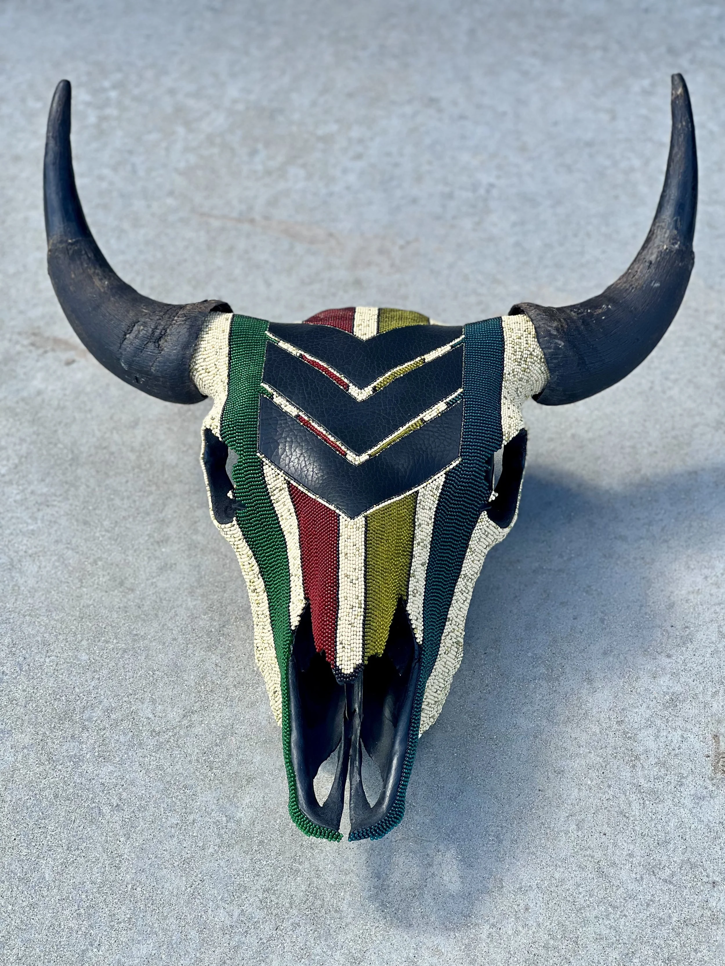 Beaded bison skull with large horns, adorned with colorful beaded patterns in green, red, yellow, black, and white.