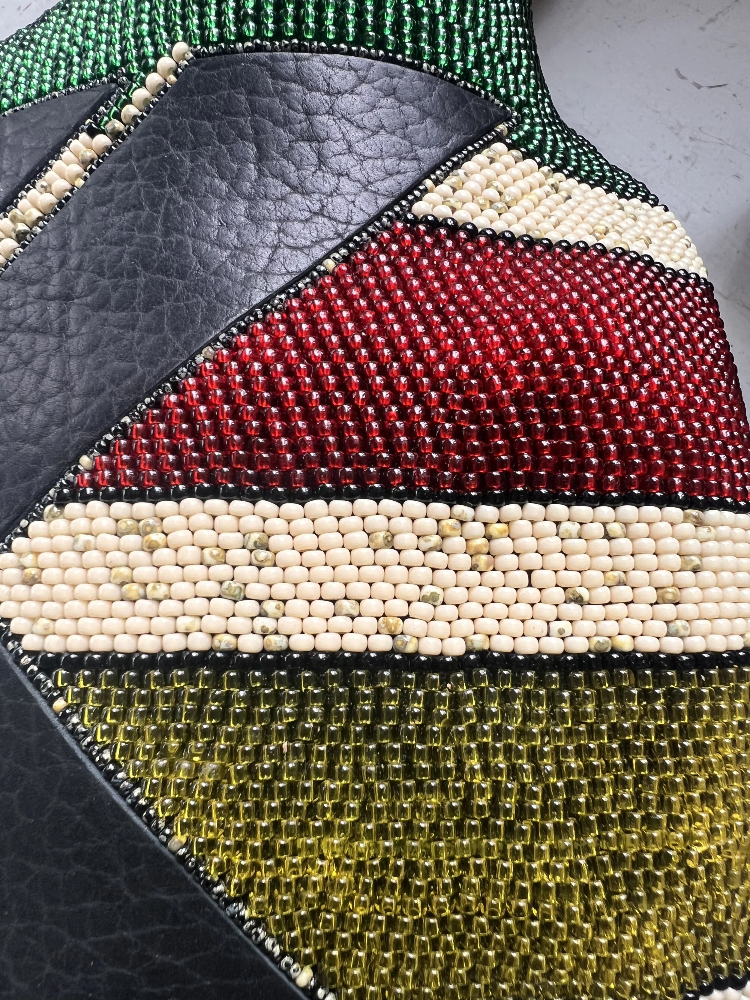 Close-up view of a colorful, diamond-studded patch on black leather, featuring sections in green, white, red, cream, and yellow beads.