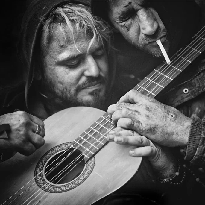 Zwei Männer spielen zusammen Gitarre, einer raucht.