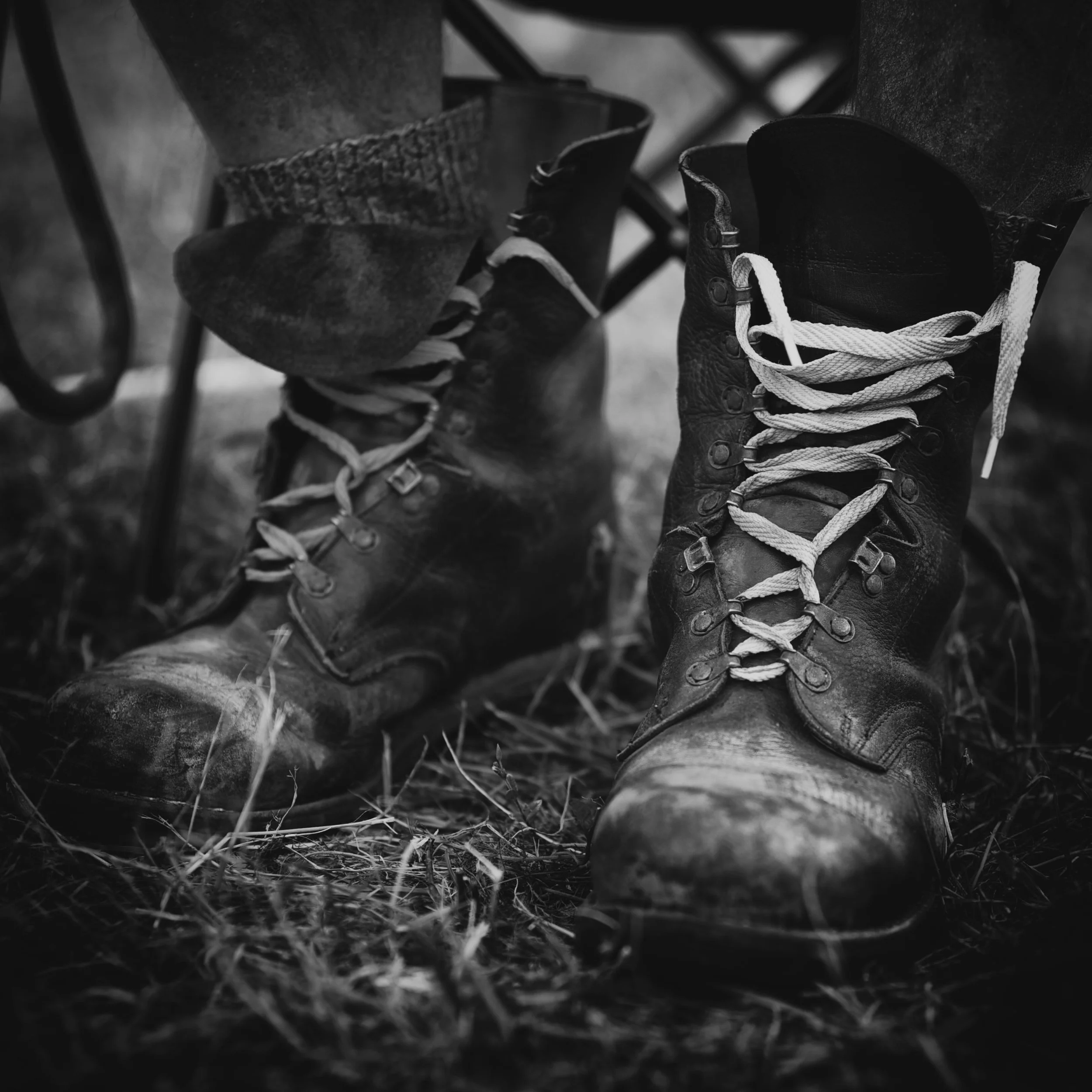 Ein Paar alte, abgenutzte Wanderschuhe im Freien, im Schwarz-Weiß-Stil fotografiert.