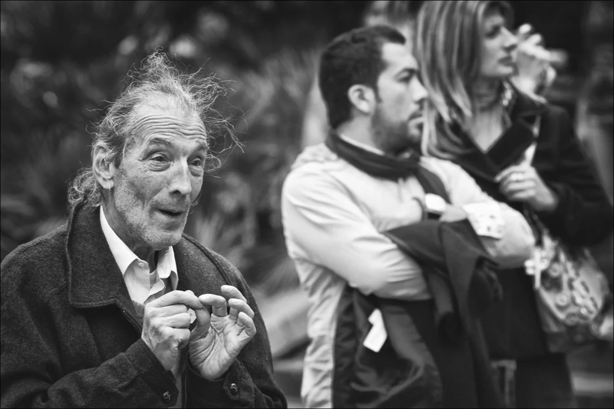 Ein älterer Mann spricht zu einer Gruppe junger Menschen, die aufmerksam zuhören. Die Szene ist schwarz-weiß.