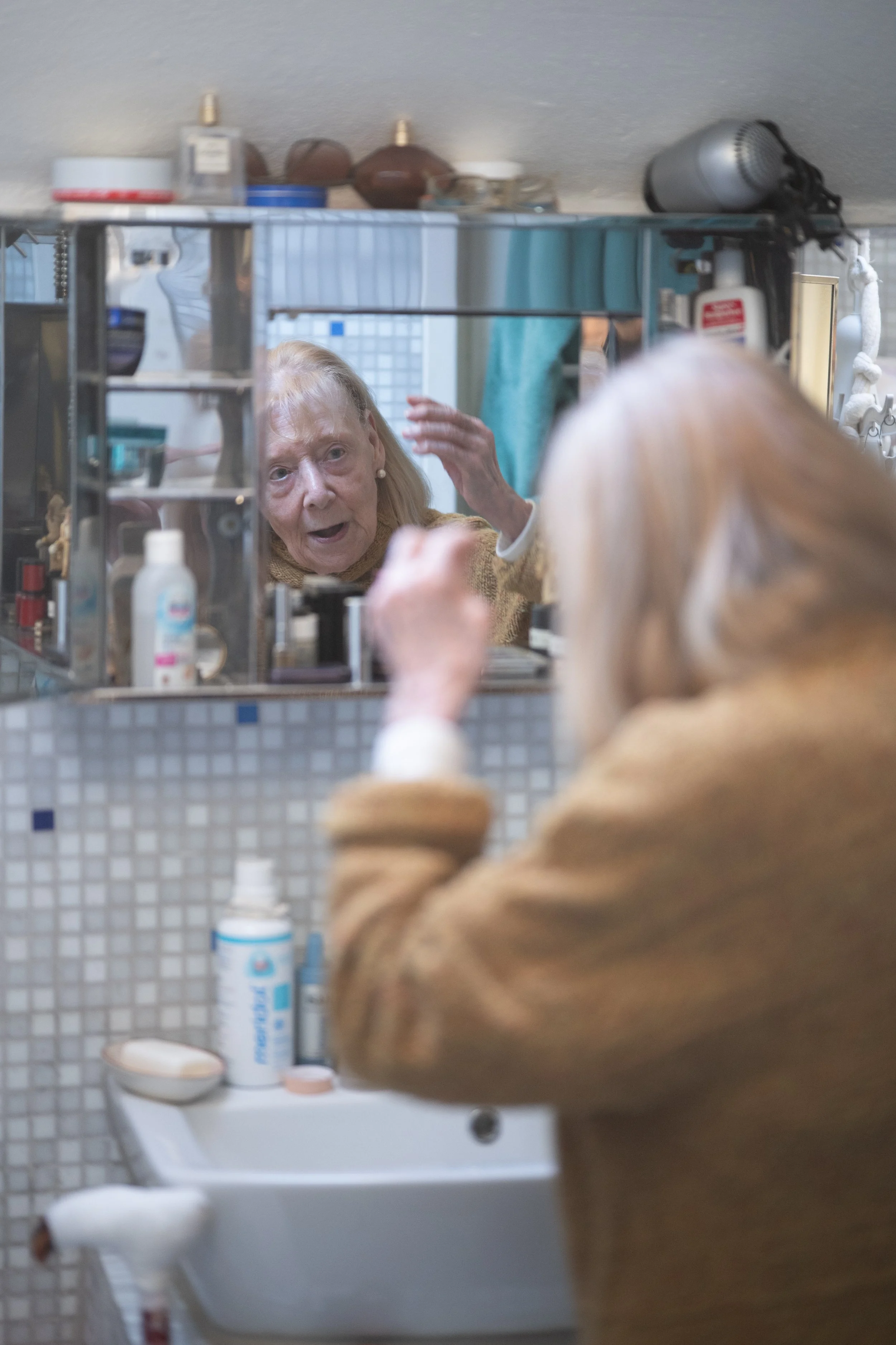 Ältere Frau schaut in einen Spiegel und frisiert ihr Haar.