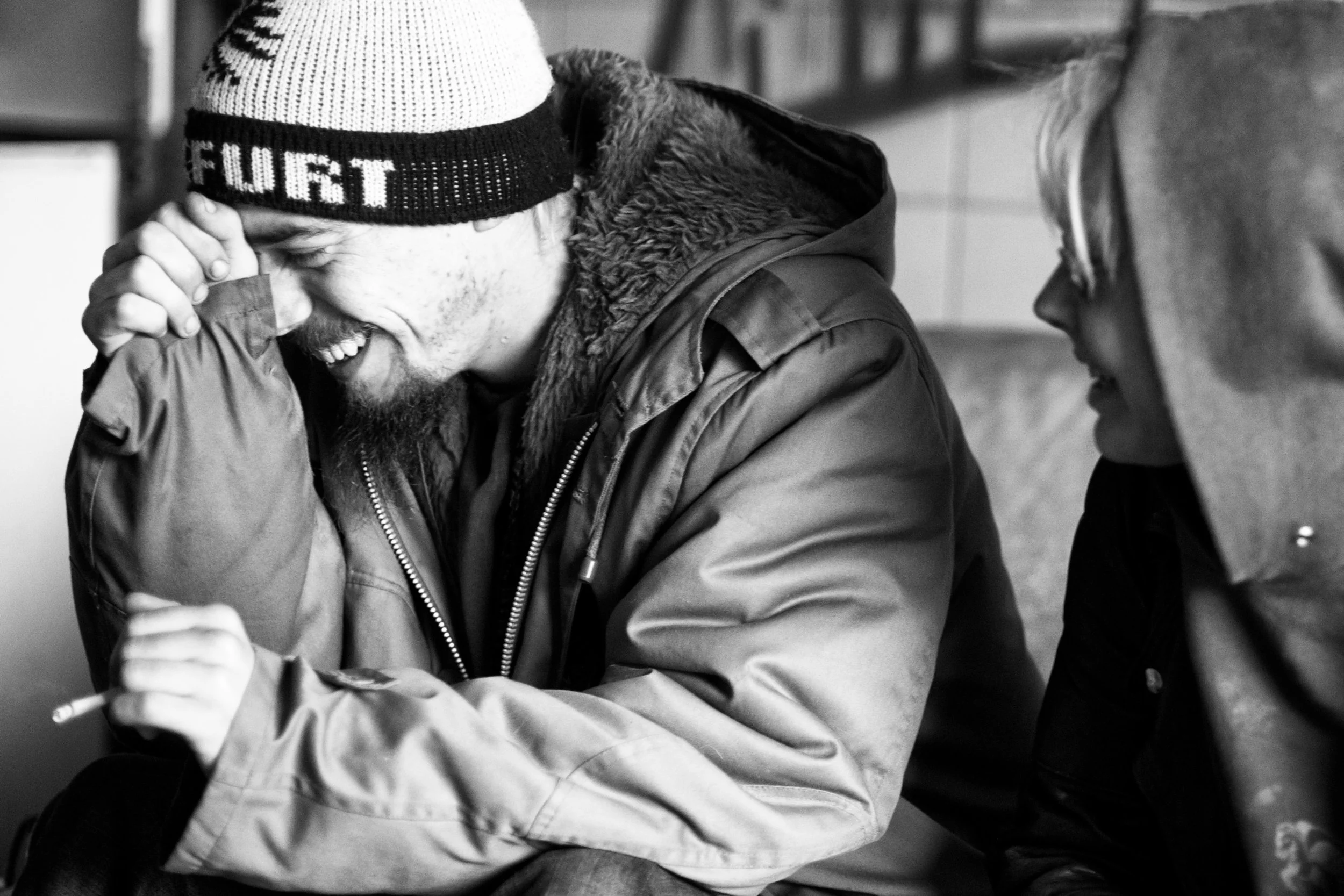 Zwei Männer lachen und unterhalten sich, einer trägt eine Mütze mit Schriftzug, der andere trägt eine Brille.