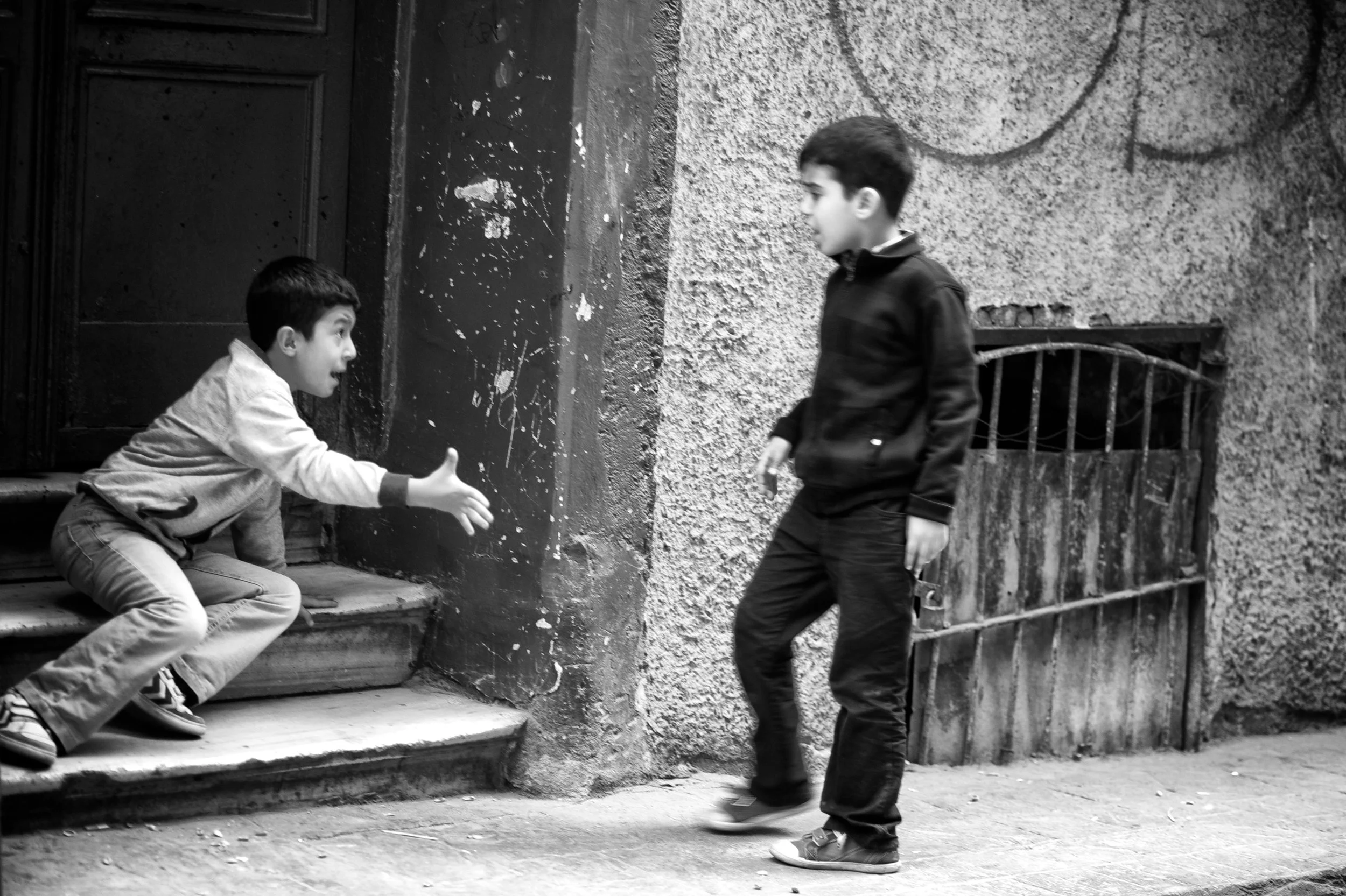 Zwei Jungen, eines auf den Stufen eines Hauses, das andere steht vor der Tür, sie begrüßen sich.