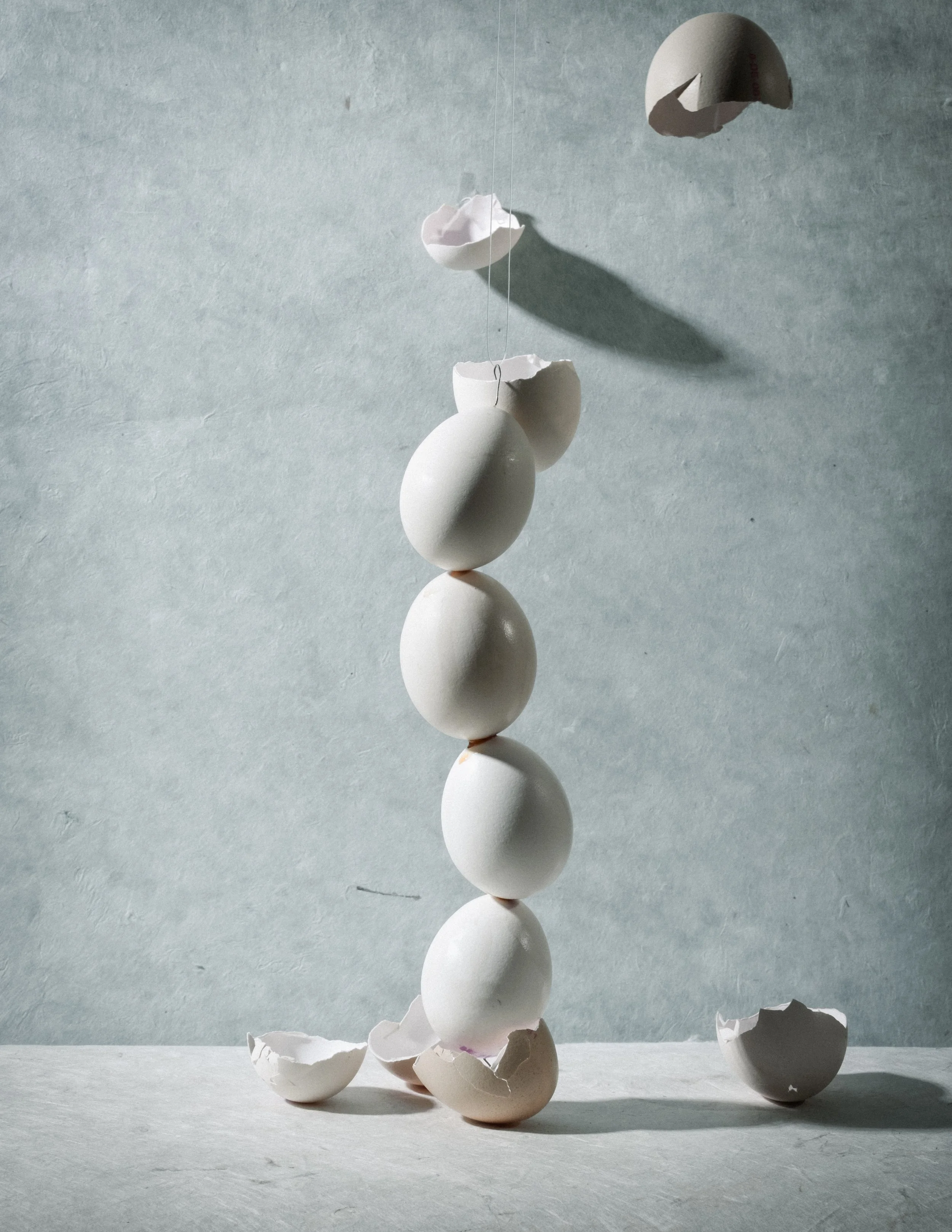 Hühnereier, die an Fäden hängen und in der Luft schwingen, über einer flachen Oberfläche mit angeschlagenen Eierschalen