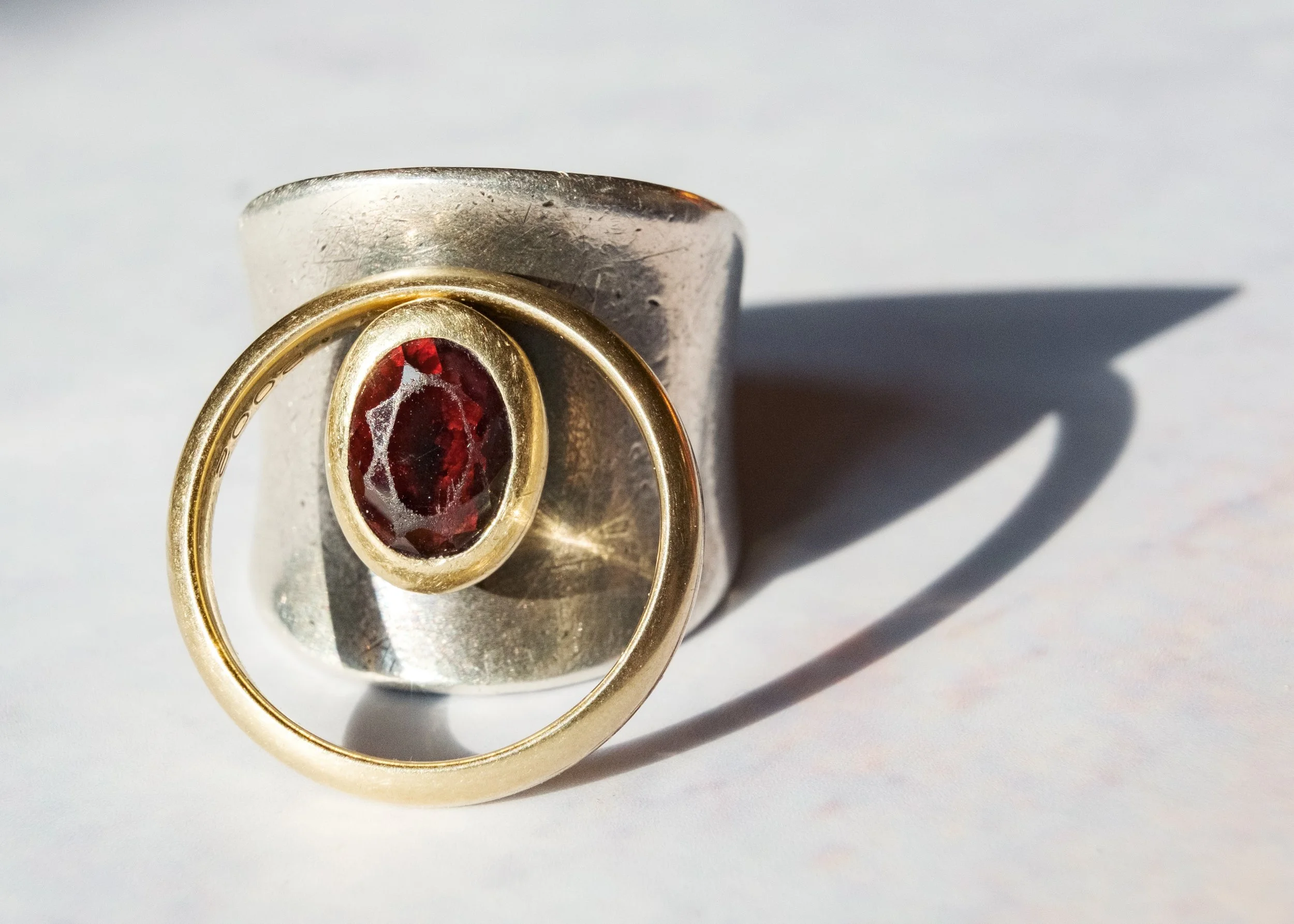 Silberring mit rotem Edelstein in Goldfassung auf weißem Hintergrund, Schatten sichtbar.