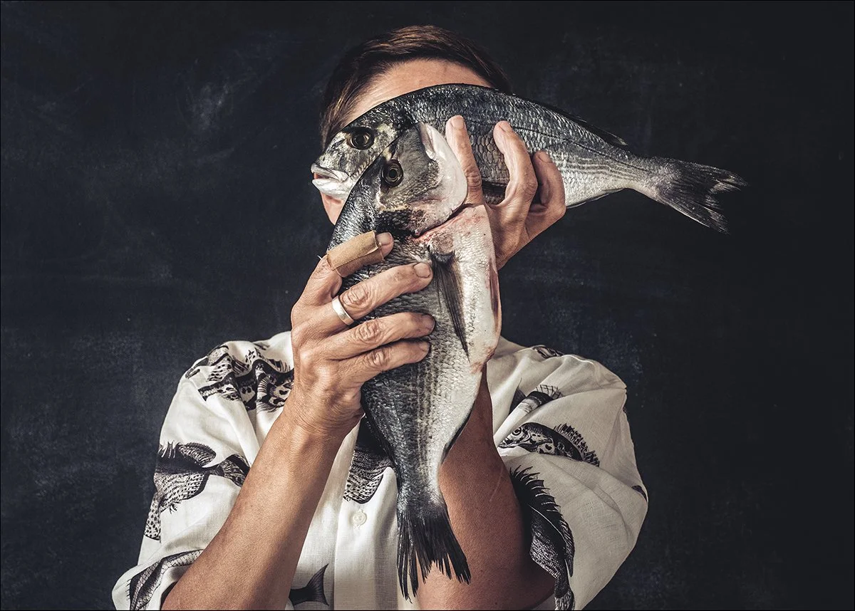 Person hält zwei Fische vor Gesicht, versteckt es teilweise