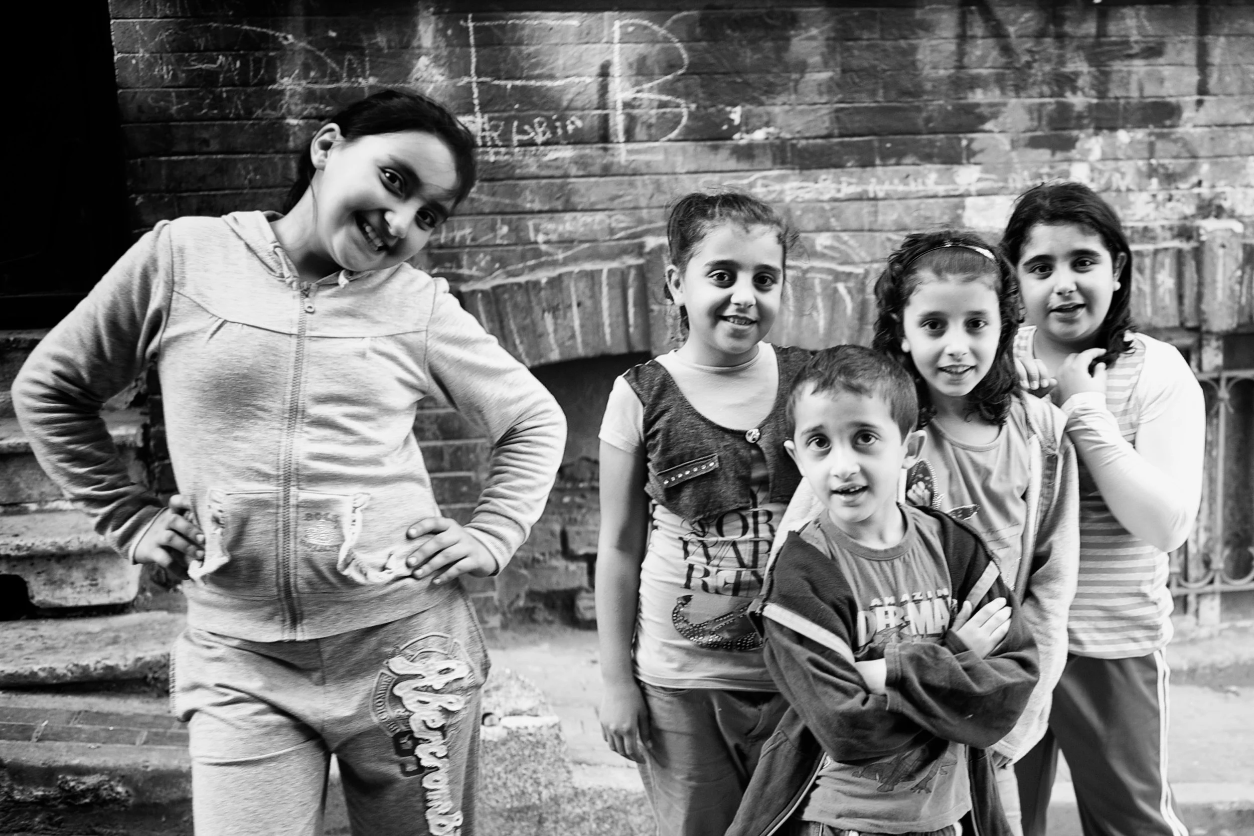 Fünf Kinder stehen vor einer Backsteinmauer, lachen und posieren für die Kamera.