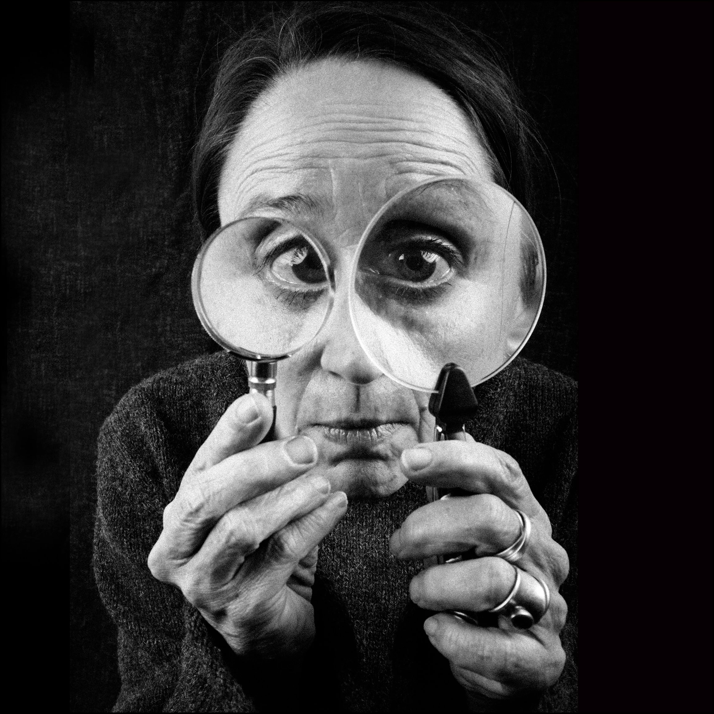 Schwarz-Weiß-Foto einer Frau, die durch zwei Lupen auf einmal schaut.