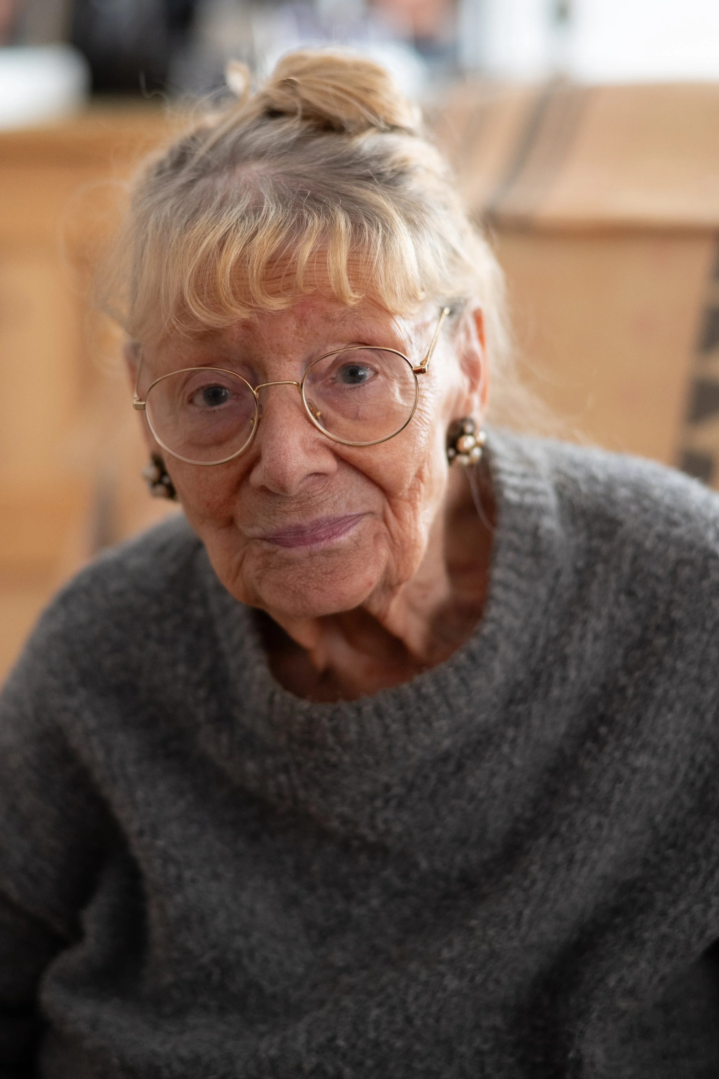 Eine ältere Frau mit Brille und grauem Pullover, die freundlich in die Kamera lächelt.