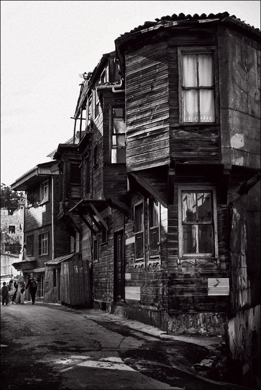 Alte, verfallende Holzhäuser an einer engen Straße in Schwarz-Weiß-Fotografie.