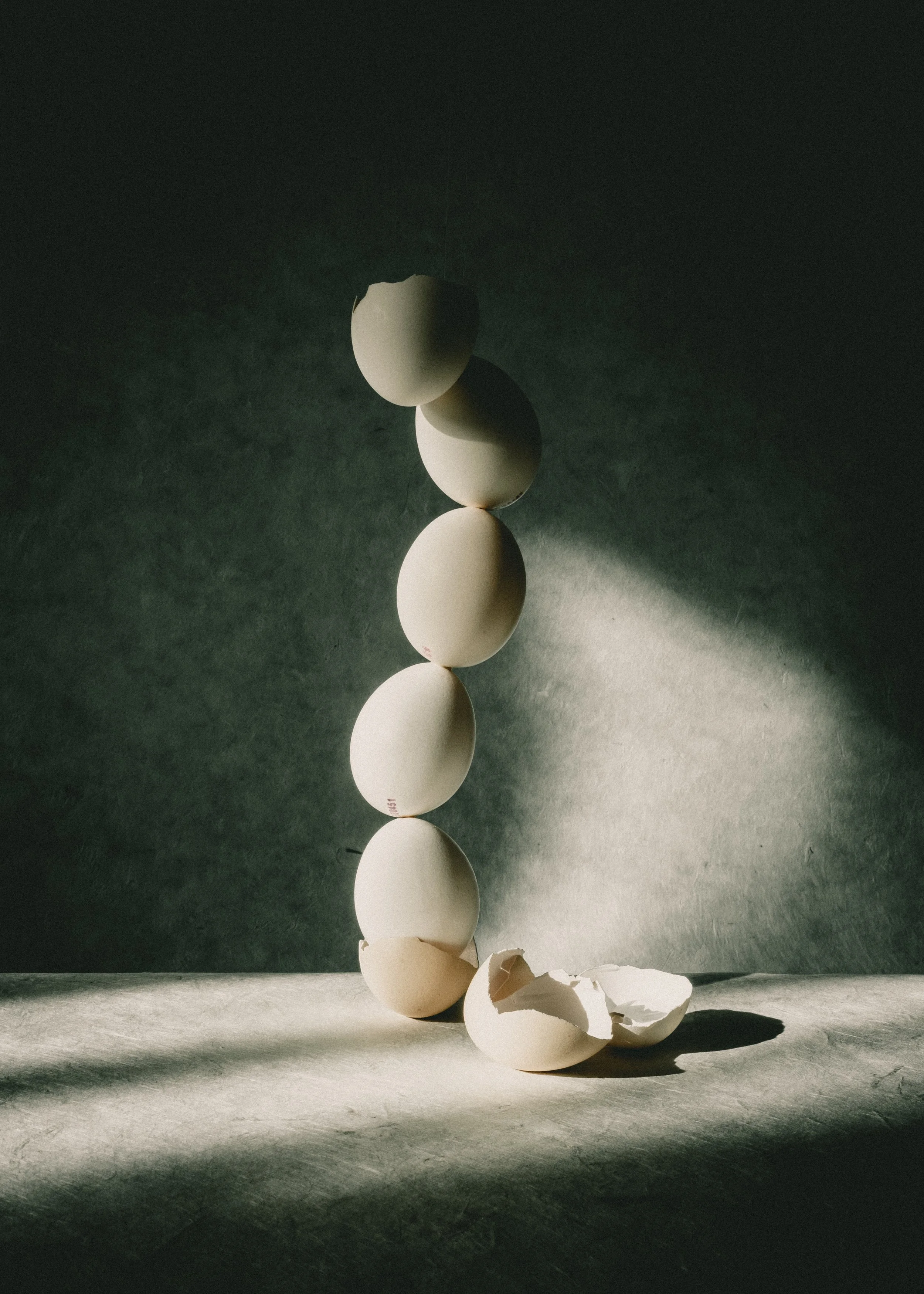 Mehrere Eier, darunter eine zerbrochene, stehen auf einem dunklen Hintergrund mit Licht- und Schatteneffekten.