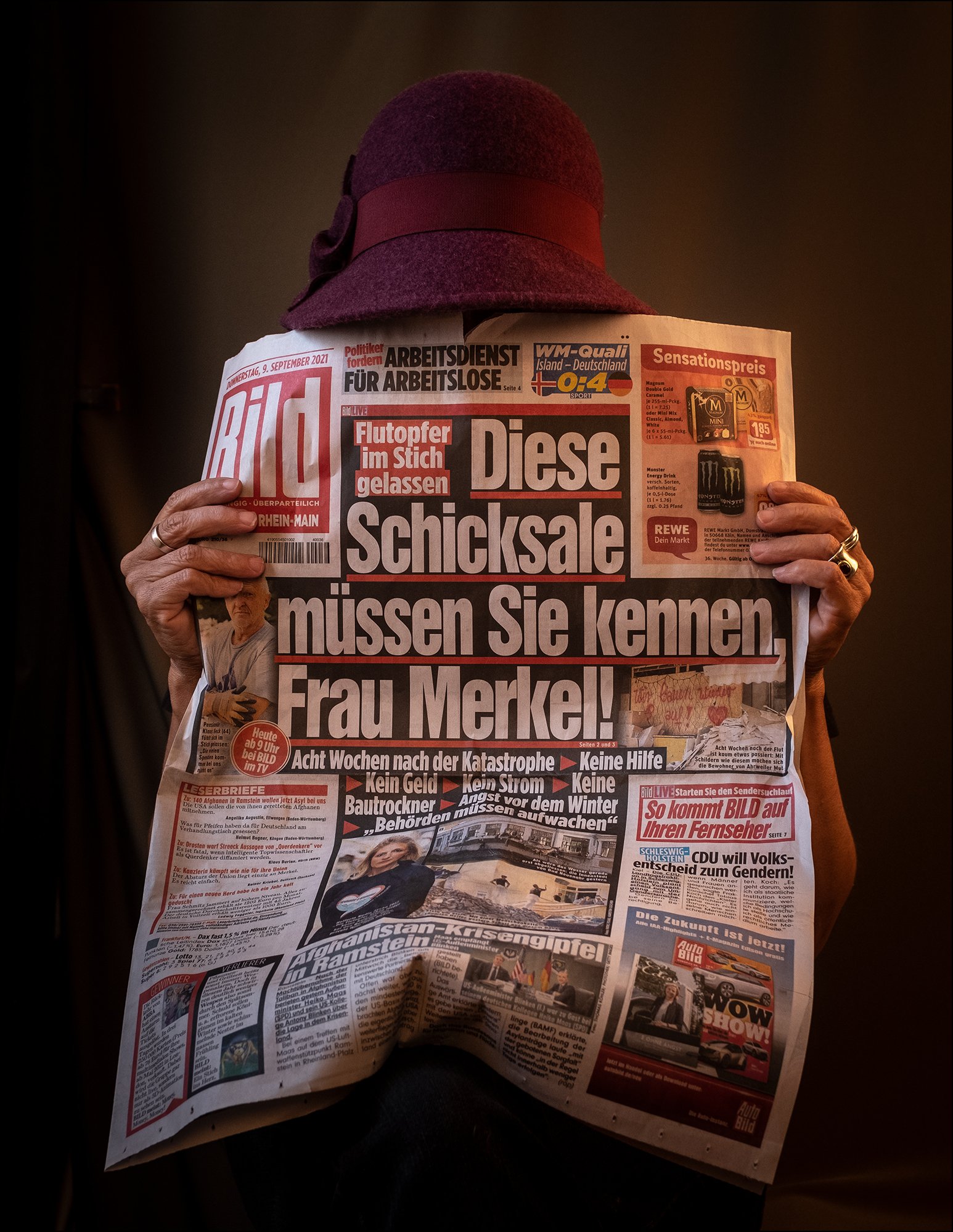 Person liest eine deutsche Zeitung, trägt einen dunklen Hut mit Schleife.