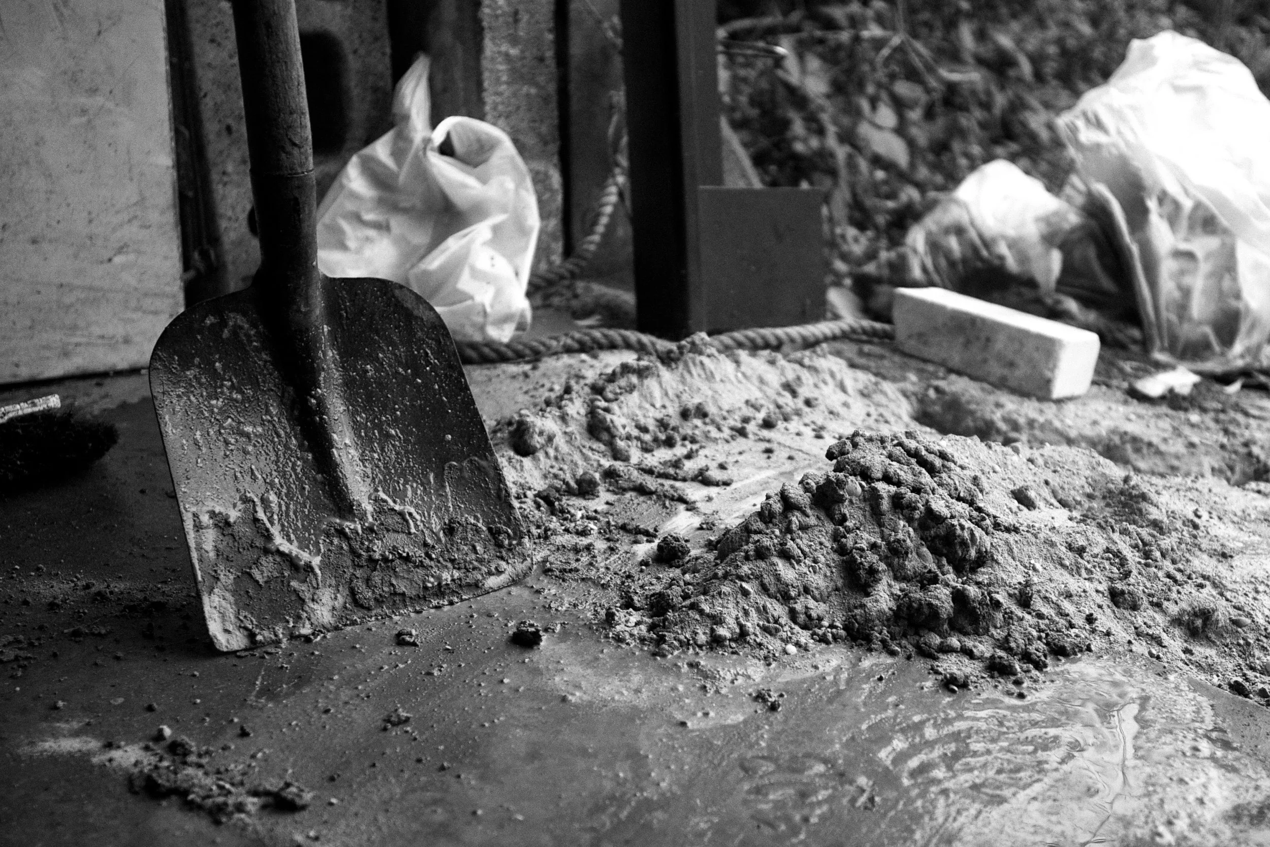 Schaufel in einer Baustelle mit Sand und Kies, hinter einigen Bauutensilien und -materialien.