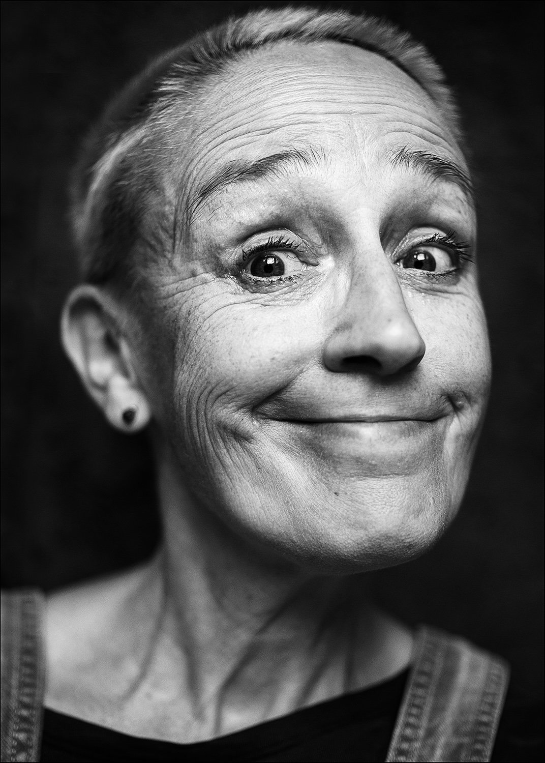 Schwarz-weiß-Fotografie eines lachenden älteren Mädchens mit hochgestecktem, grauen Haar, sichtbaren Falten und hellen Augen.