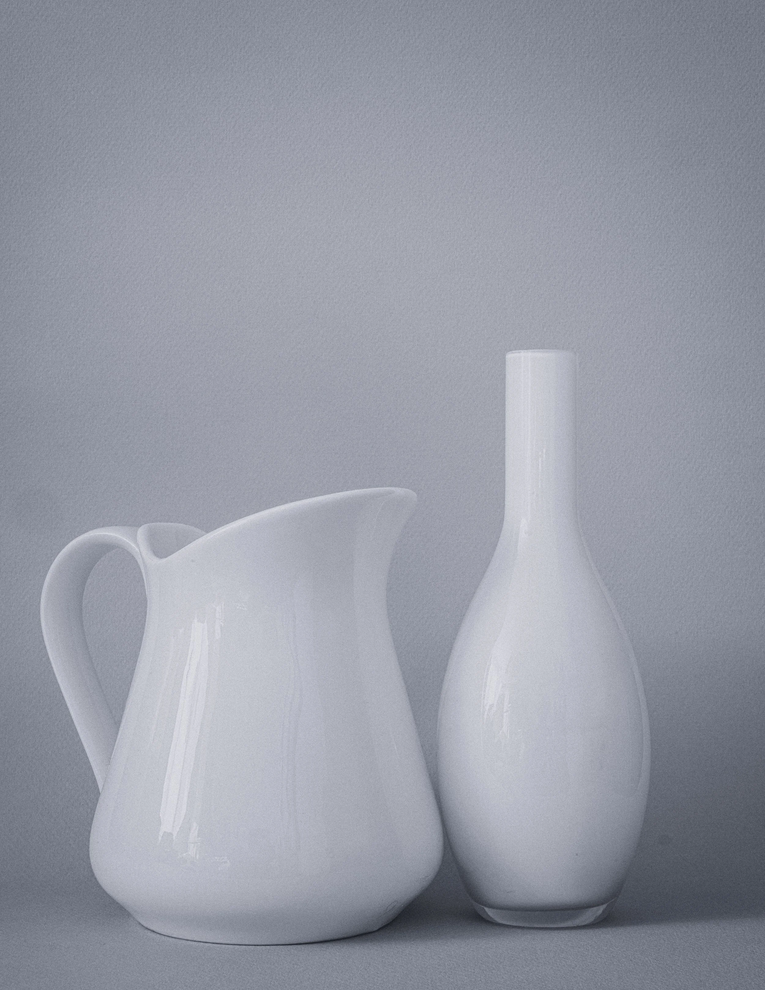 Zwei weiße Keramikvasen auf einem grauen Hintergrund, eine große mit kurzem Hals und eine kleinere mit langem, schlankem Hals.