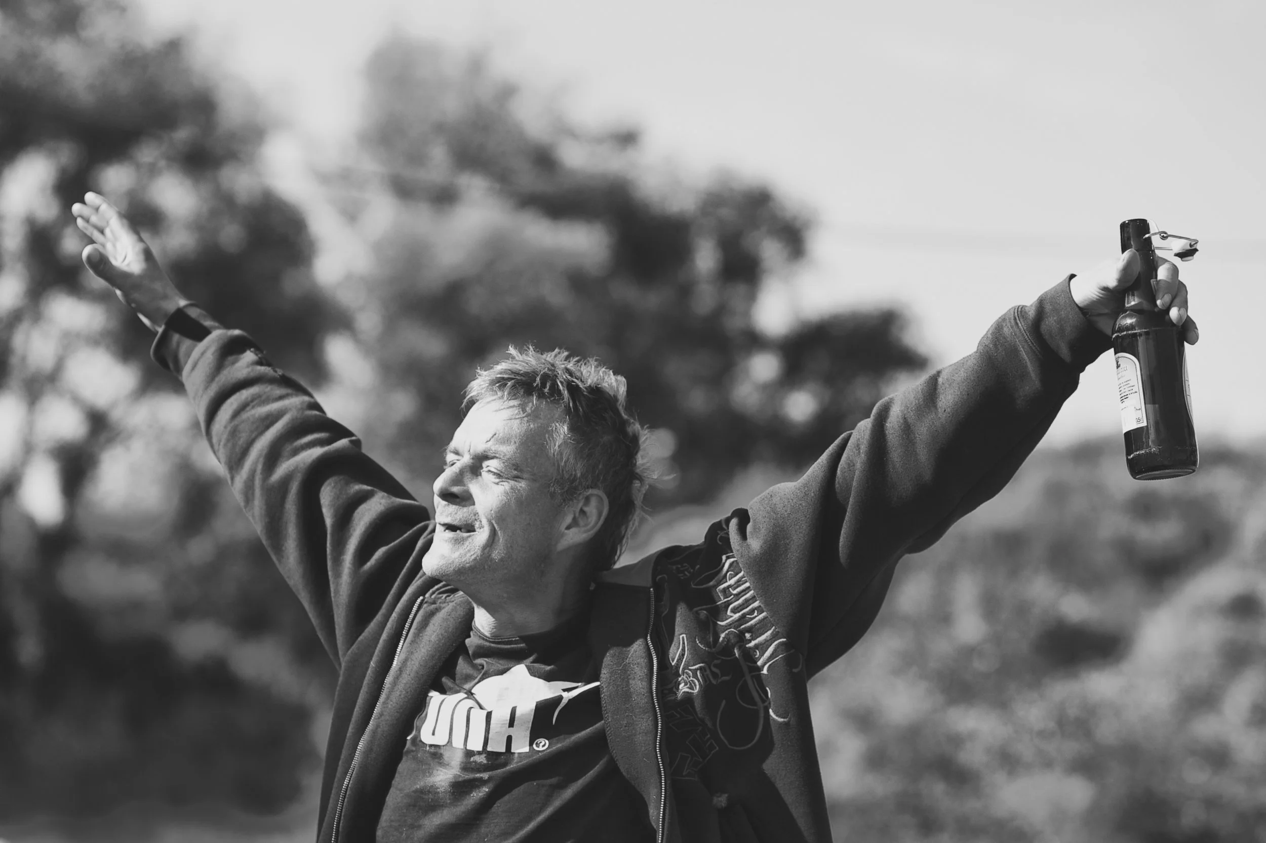 Ein Mann mit einem Rucksack, der die Arme in die Luft streckt, in einer Outdoor-Landschaft, schwarz-weiß Fotografie.