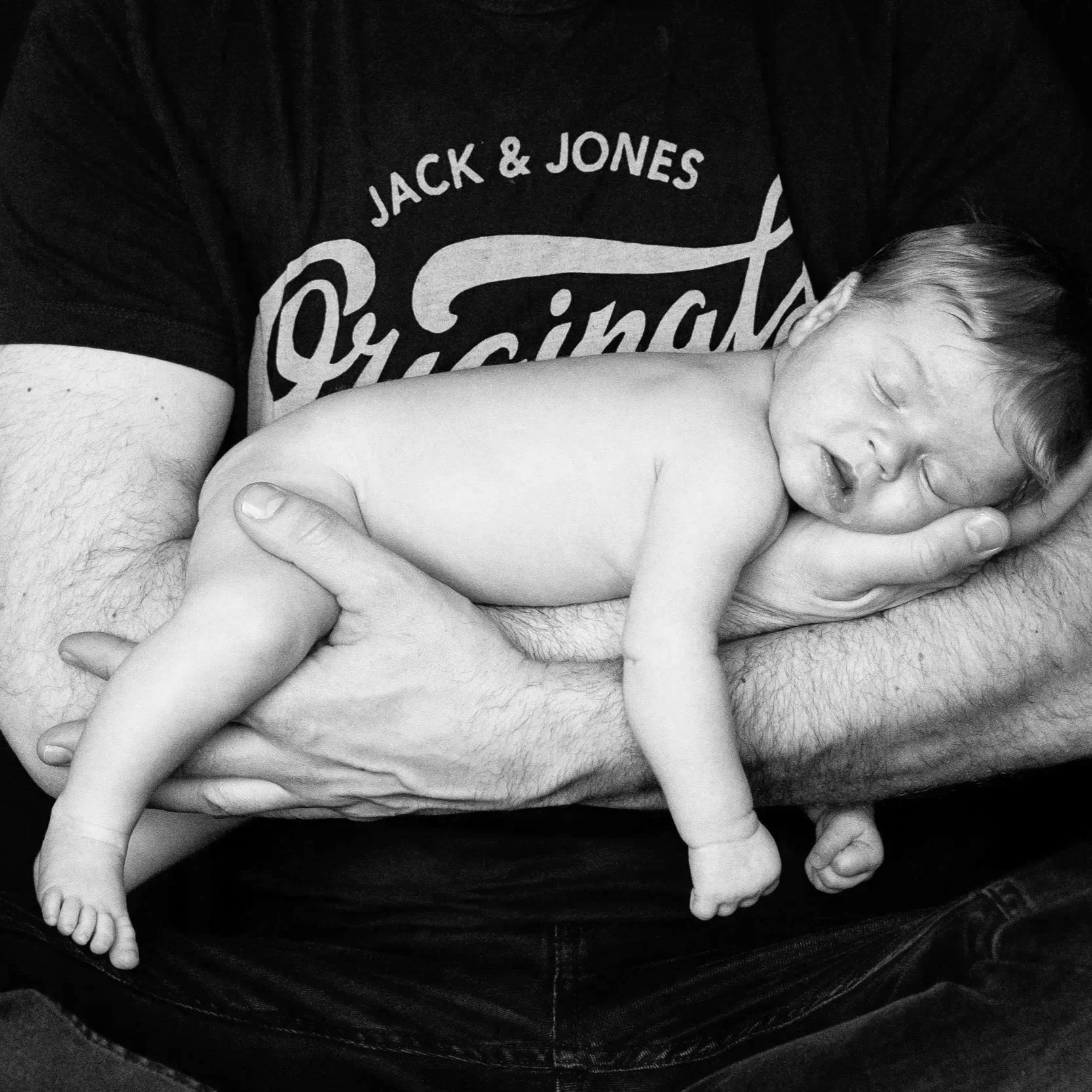 Neugeborenes liegt friedlich in den Armen des Vaters