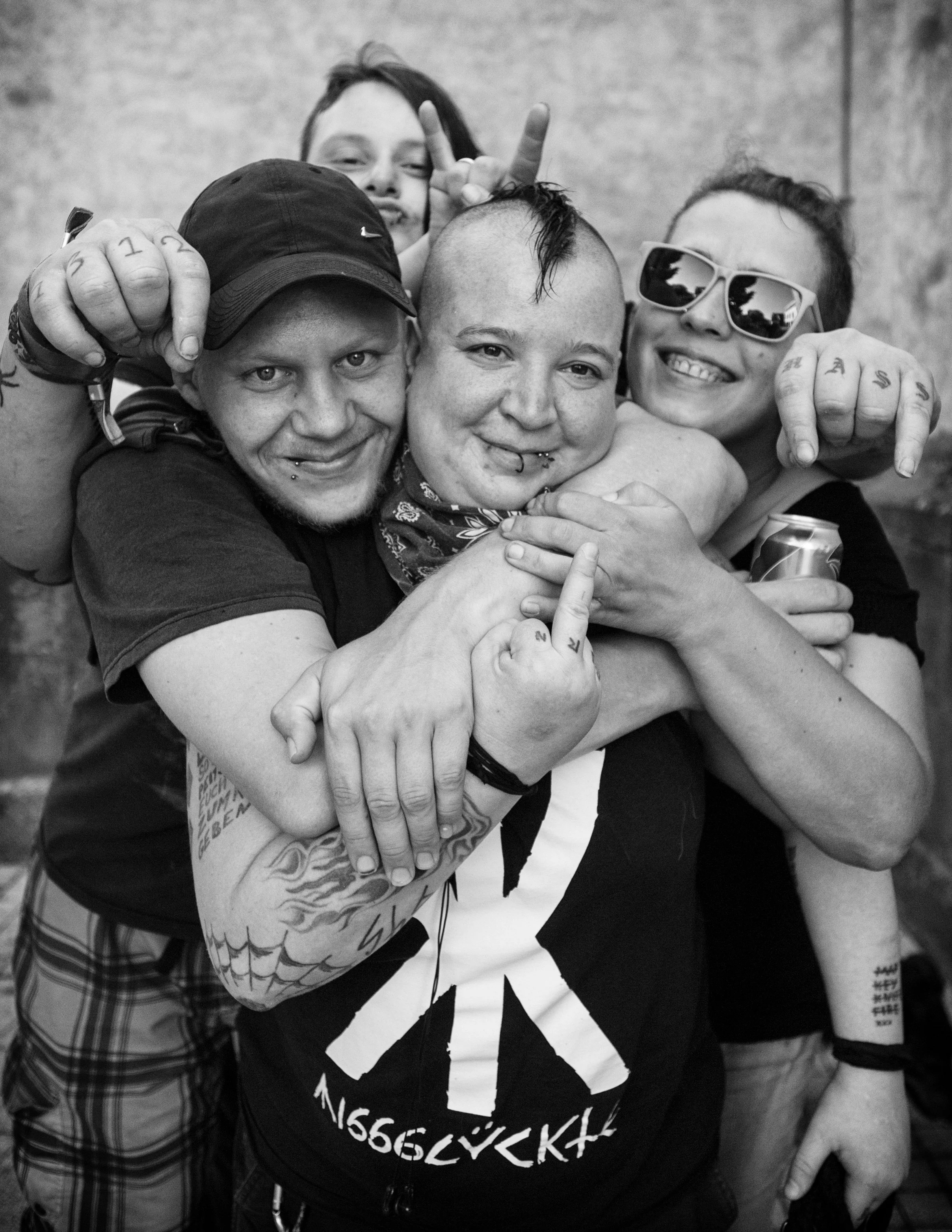 Vier junge Menschen, die sich umarmen und Spaß haben, in Schwarz-Weiß-Fotografie. Zwei tragen Sonnenbrillen, einen trägt eine Mütze, sie wirken glücklich und ausgelassen.